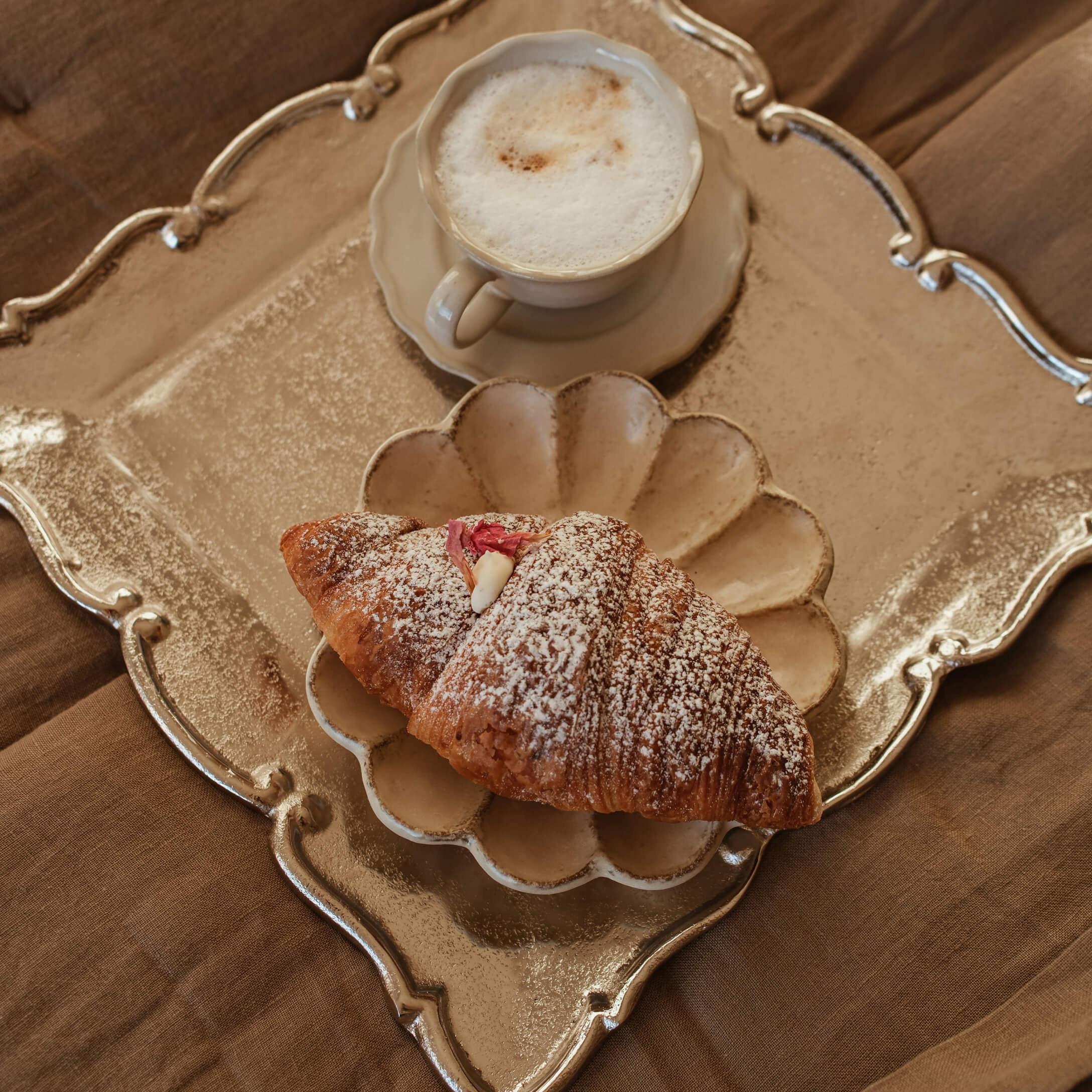 Tasse de cappuccino crème et croissant saupoudré de sucre sur assiette beige et plateau doré