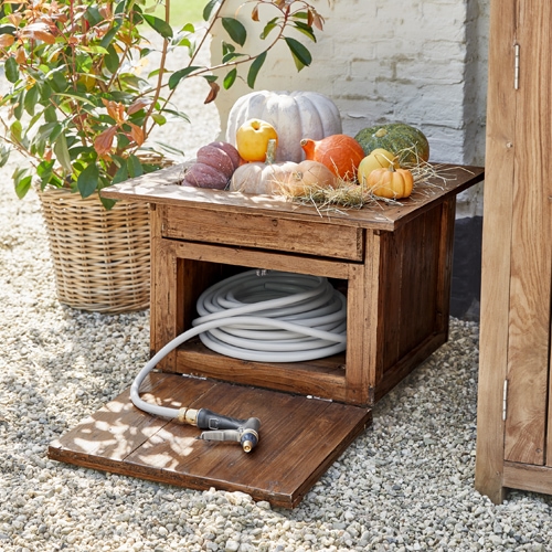 Coffre de jardin en bois avec tuyau blanc et citrouilles décoratives sur sol en gravier