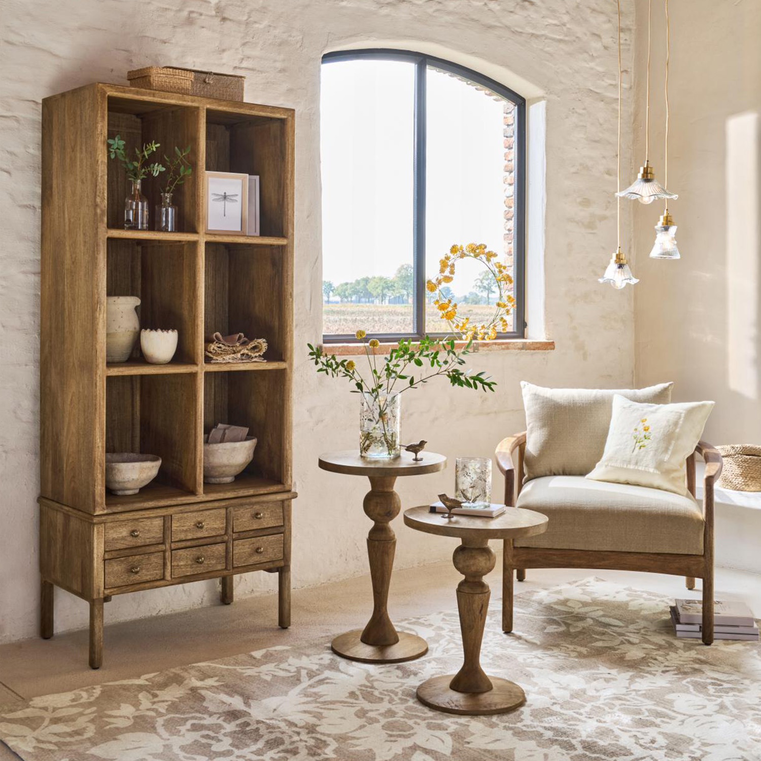 Bibliothèque en bois naturel avec tiroirs et tables d'appoint dans un salon lumineux avec fauteuil beige