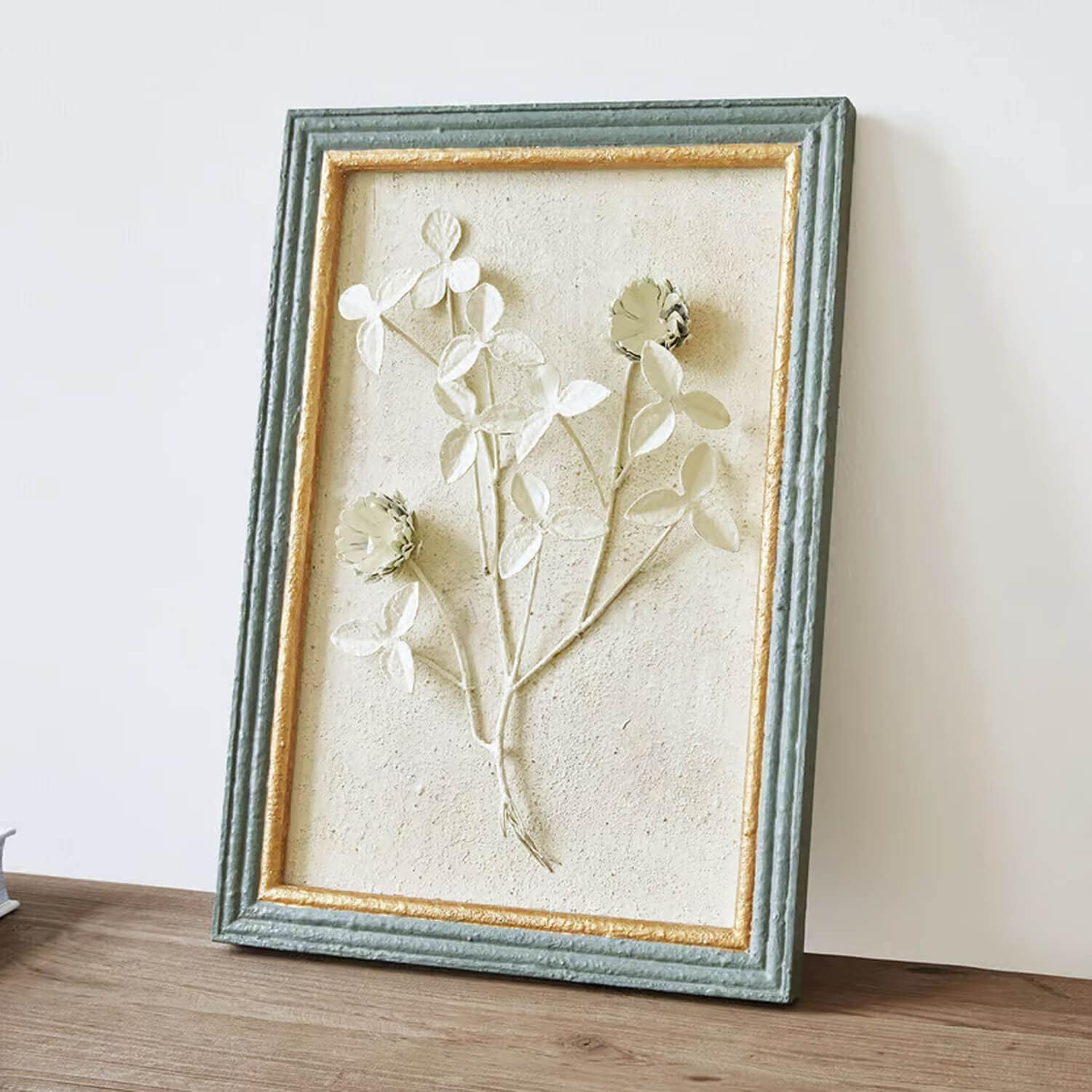 Relief floral décoratif encadré avec texture verte et dorée sur fond beige clair