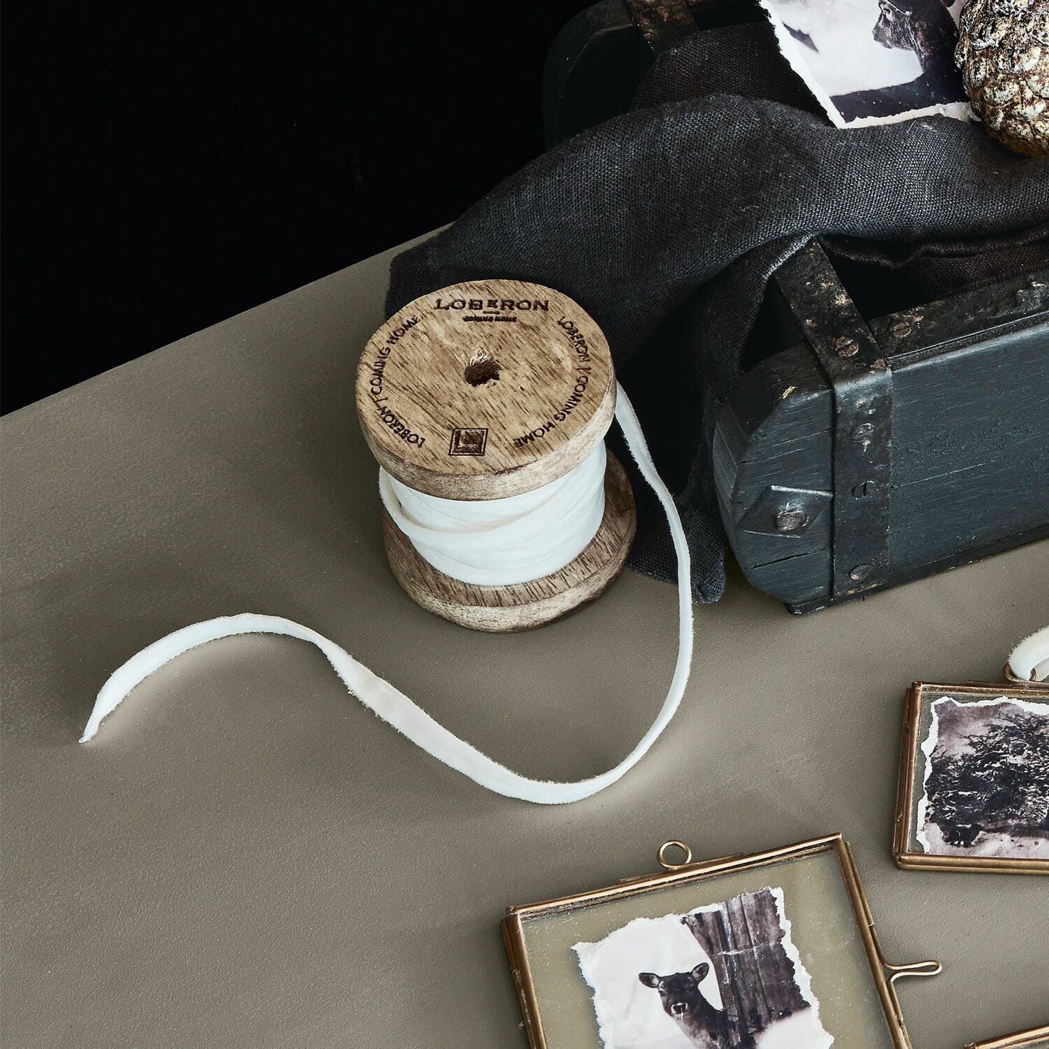 Ruban de velours Olessa Bobine en bois avec tissu blanc sur table près d'une boîte noire et cadres photo décoratifs
