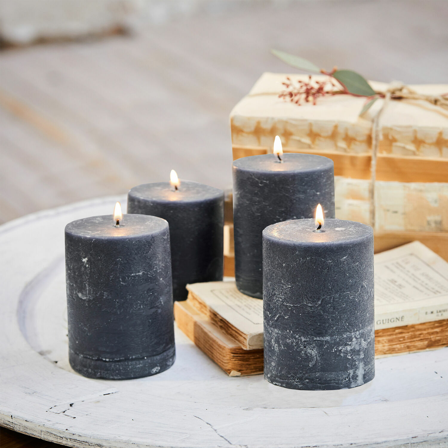 Lot de 4 bougies Virrans Quatre bougies noires en cire sur une table en bois blanc avec des livres et un cadeau
