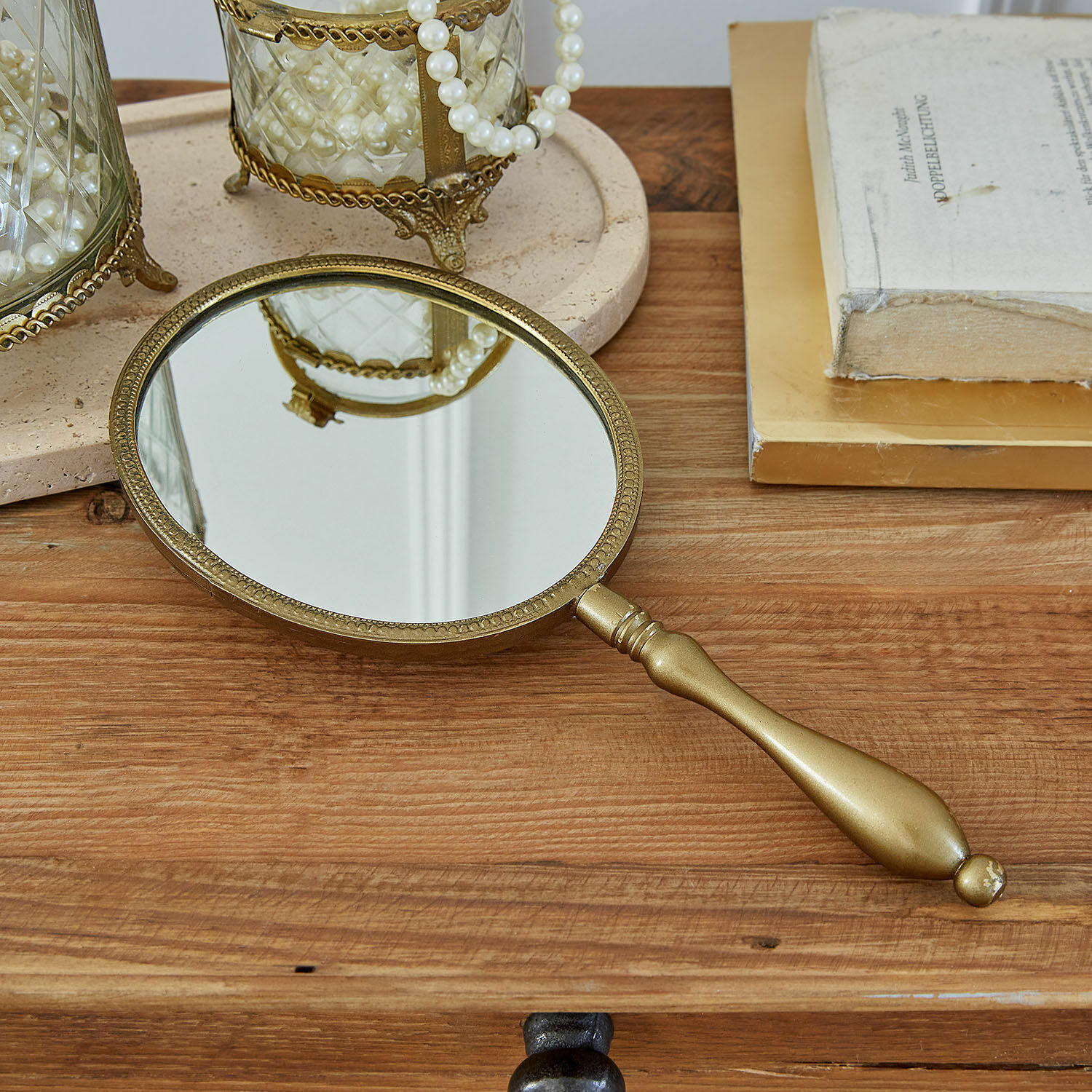 Miroir à main Aravelle Miroir à main doré avec cadre décoratif sur une table en bois avec livres et perles