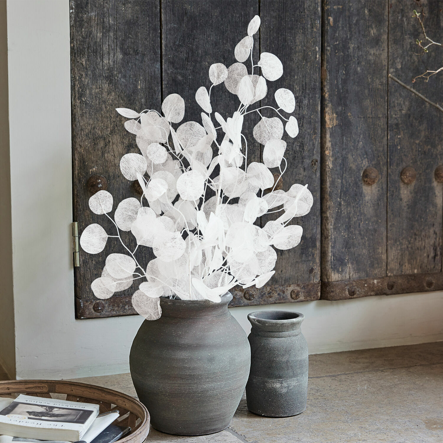 Lot de 3 fleurs décoratives Tilly Grand vase en céramique noire avec branches décoratives blanches devant une porte en bois rustique