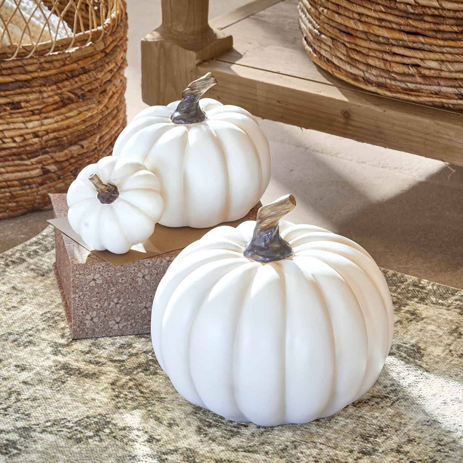 Citrouilles décoratives blanches en plastique avec tiges brunes sur tapis et table en bois