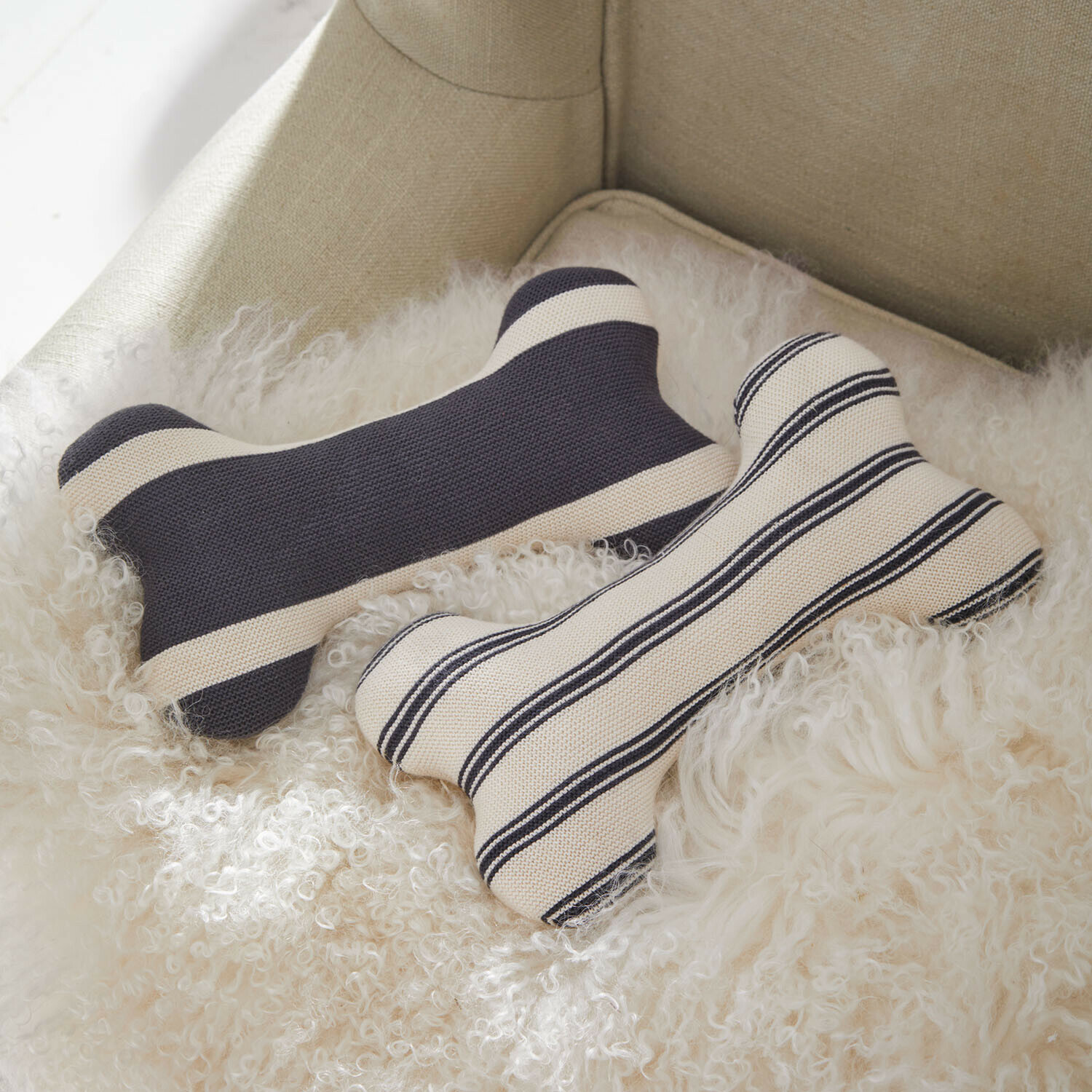 Lot de 2 coussins pour animaux Snuffa Deux coussins en forme d'os en coton rayé noir et blanc posés sur une fourrure douce