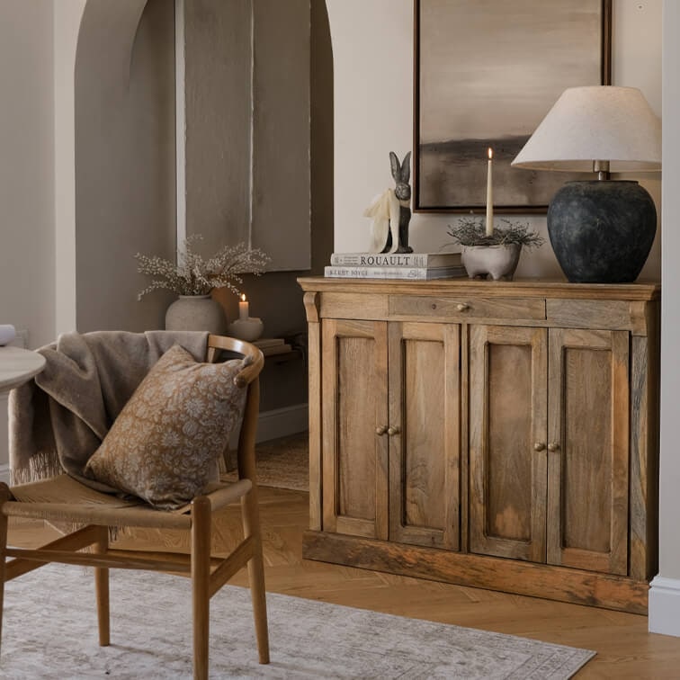 Buffet en bois naturel avec lampe et décorations dans un salon chaleureux avec chaise et coussin