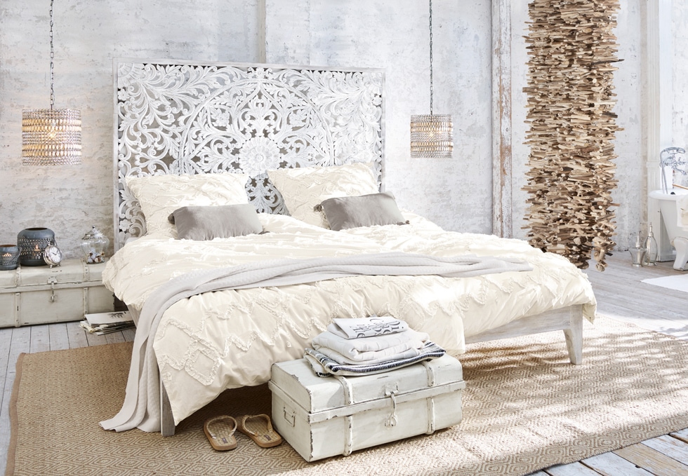 Chambre bohème avec lit blanc sculpté, literie crème et décorations naturelles en bois et rotin