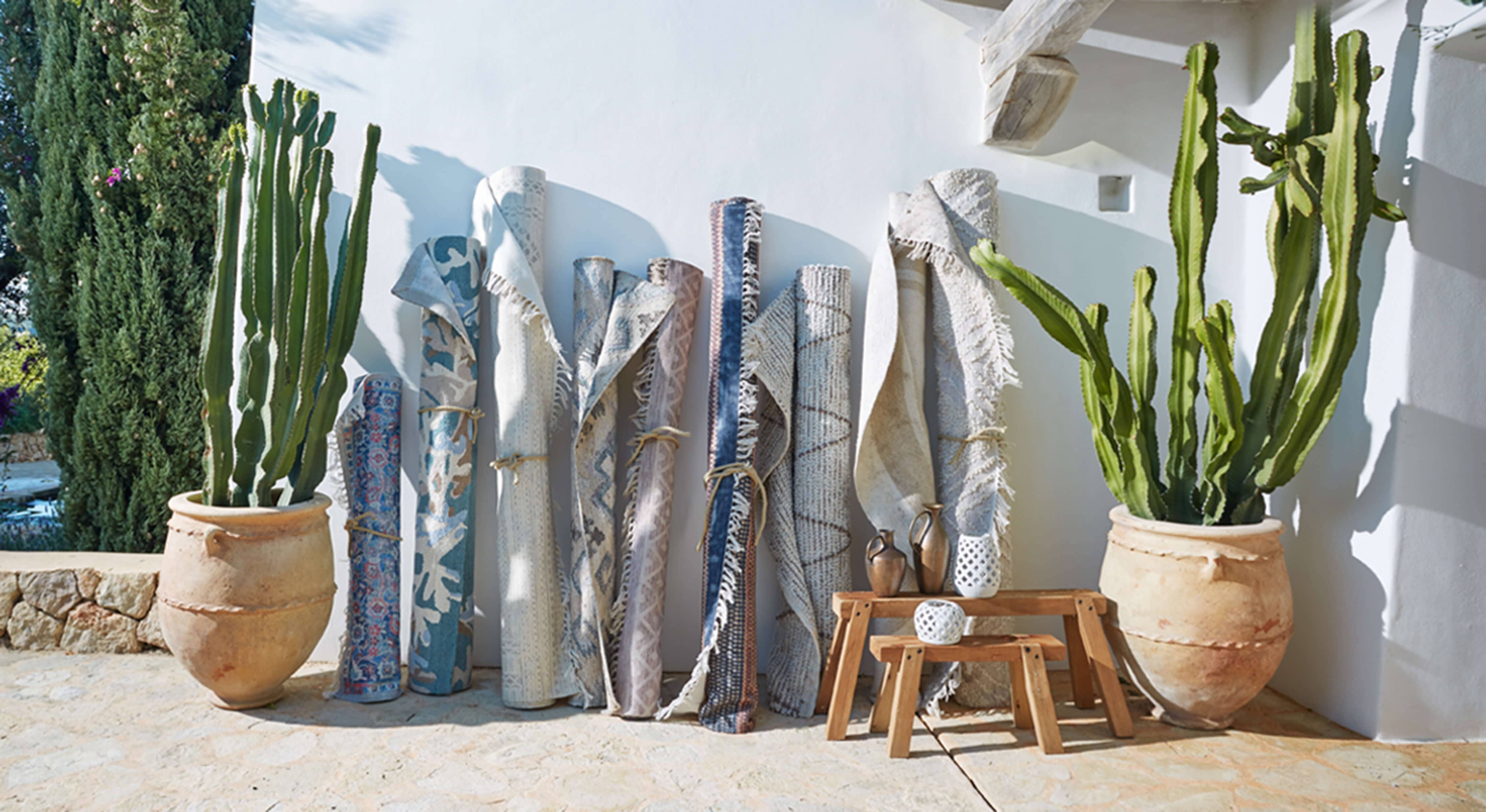 Ensemble de tapis roulés bleu et beige appuyés contre un mur blanc avec des pots en terre cuite et cactus