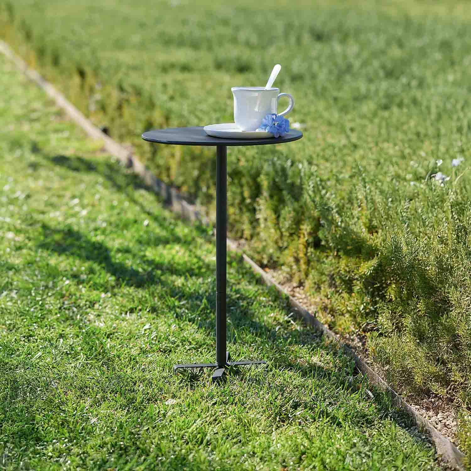Petite table de jardin noire en métal avec tasse blanche et fleur bleue sur l'herbe