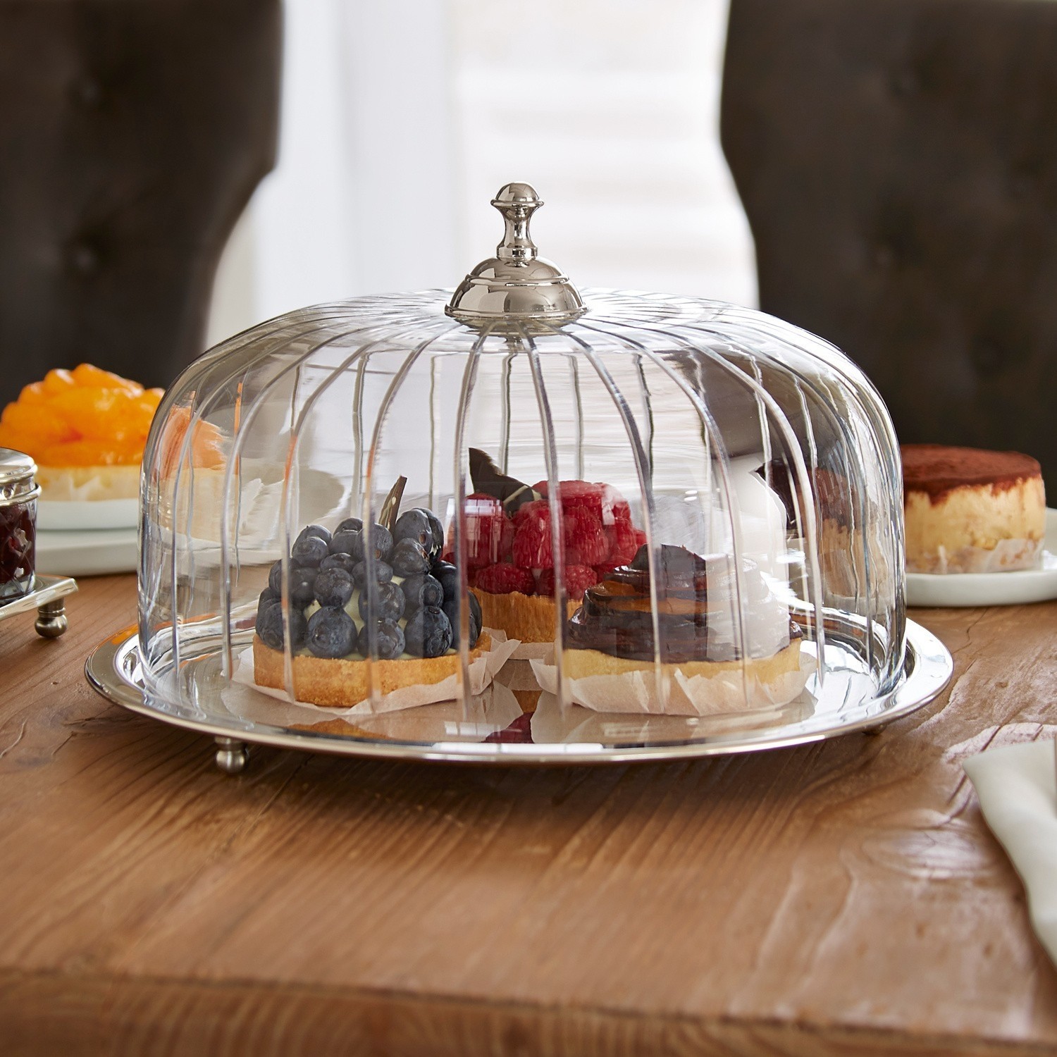 Cloche à gâteau Allaire Cloche en verre avec poignée en métal sur table en bois, contenant des tartes aux fruits variés