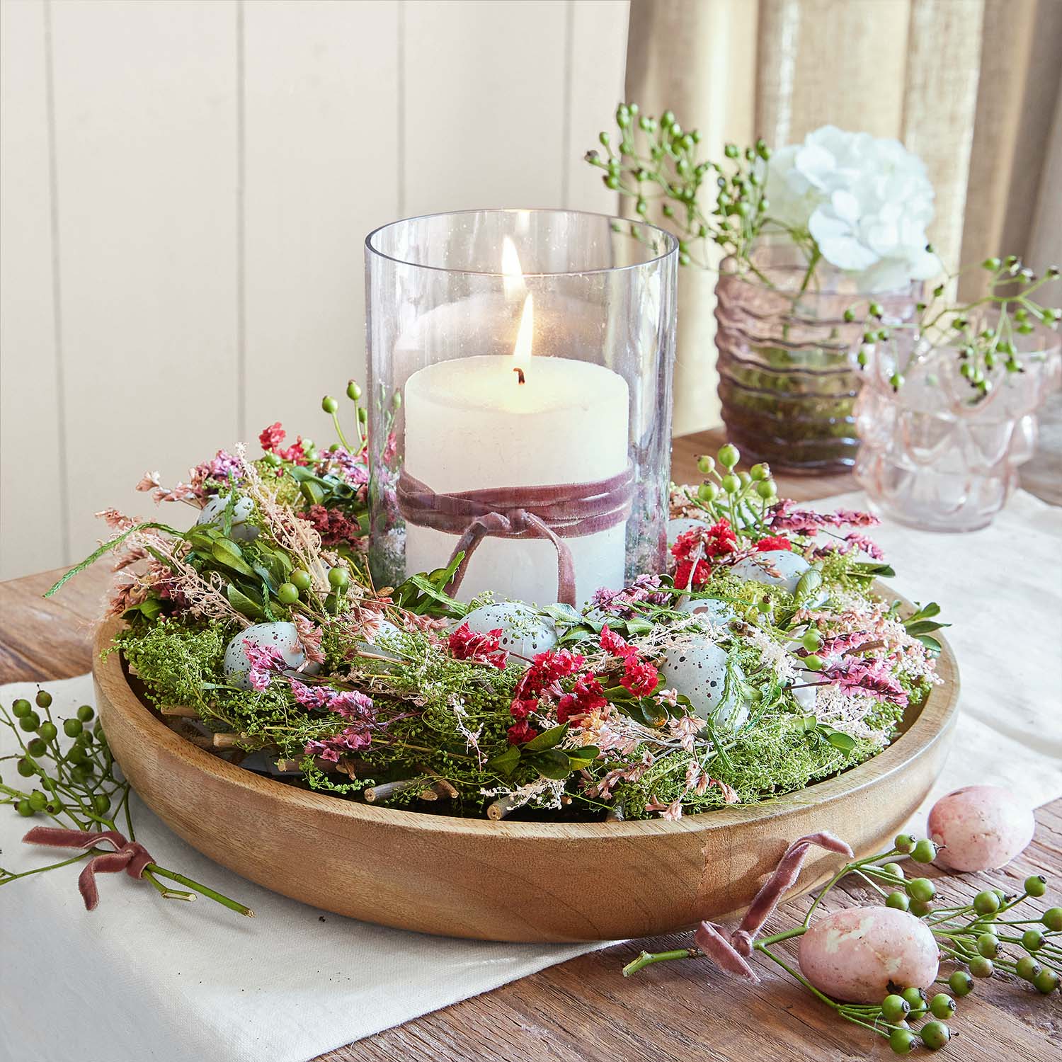 Bougeoir en bois avec bougie blanche dans un verre entouré de fleurs et œufs décoratifs colorés