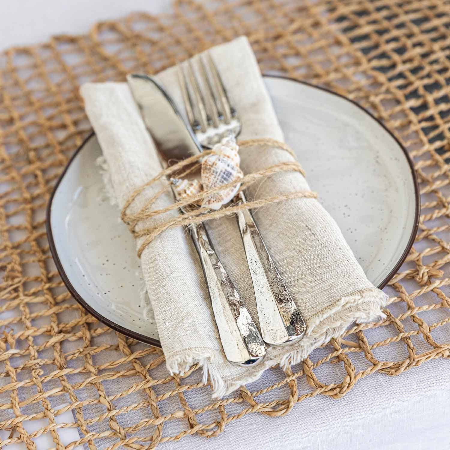 Couverts en acier inoxydable sur serviette en lin avec coquillage, assiette en céramique et napperon tressé