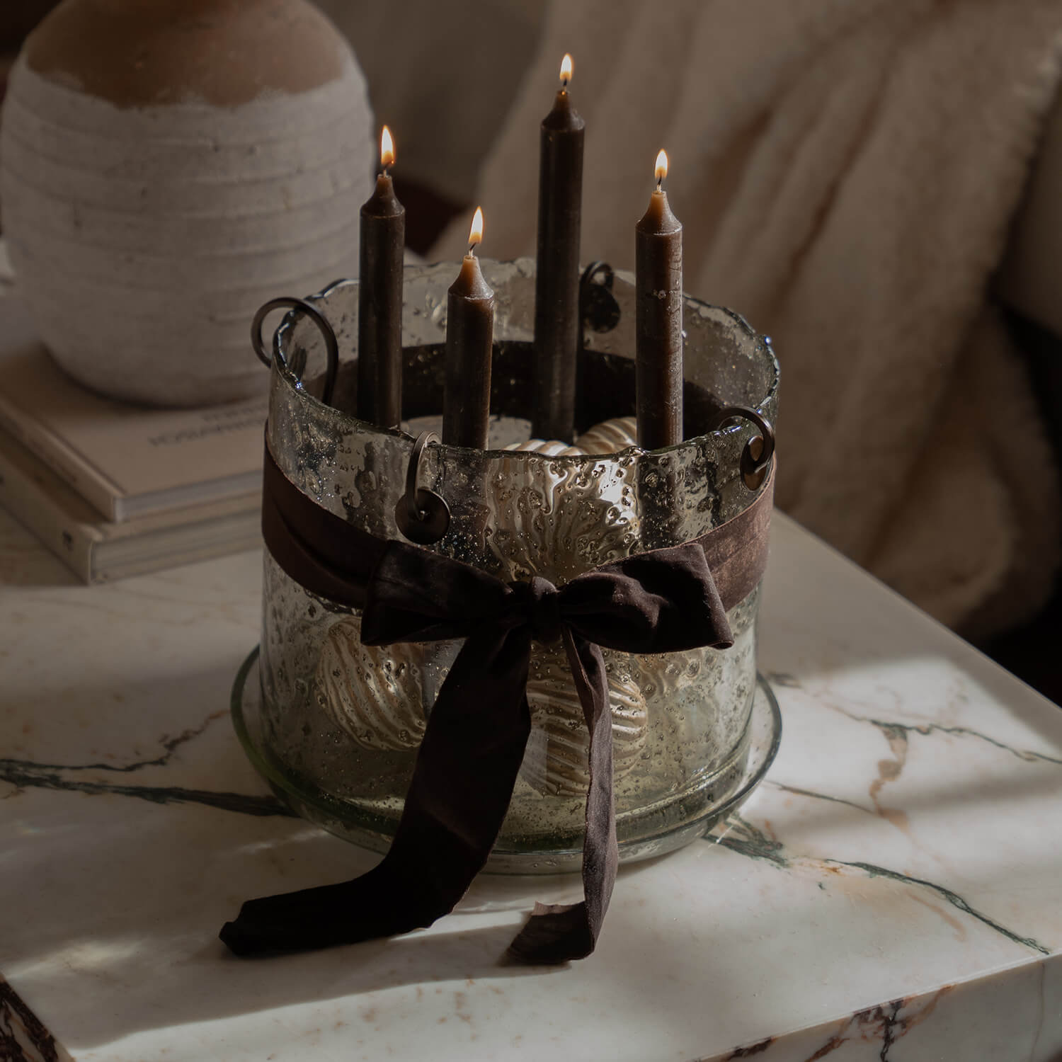 Bougeoir en verre avec quatre bougies marron et un ruban décoratif sur une table en marbre