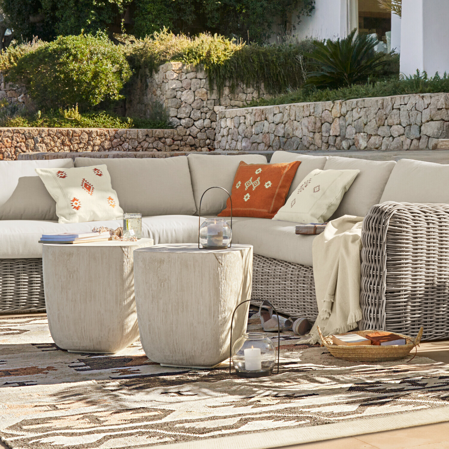 Ensemble de mobilier d'extérieur avec canapé en rotin beige et deux tables basses claires sur terrasse