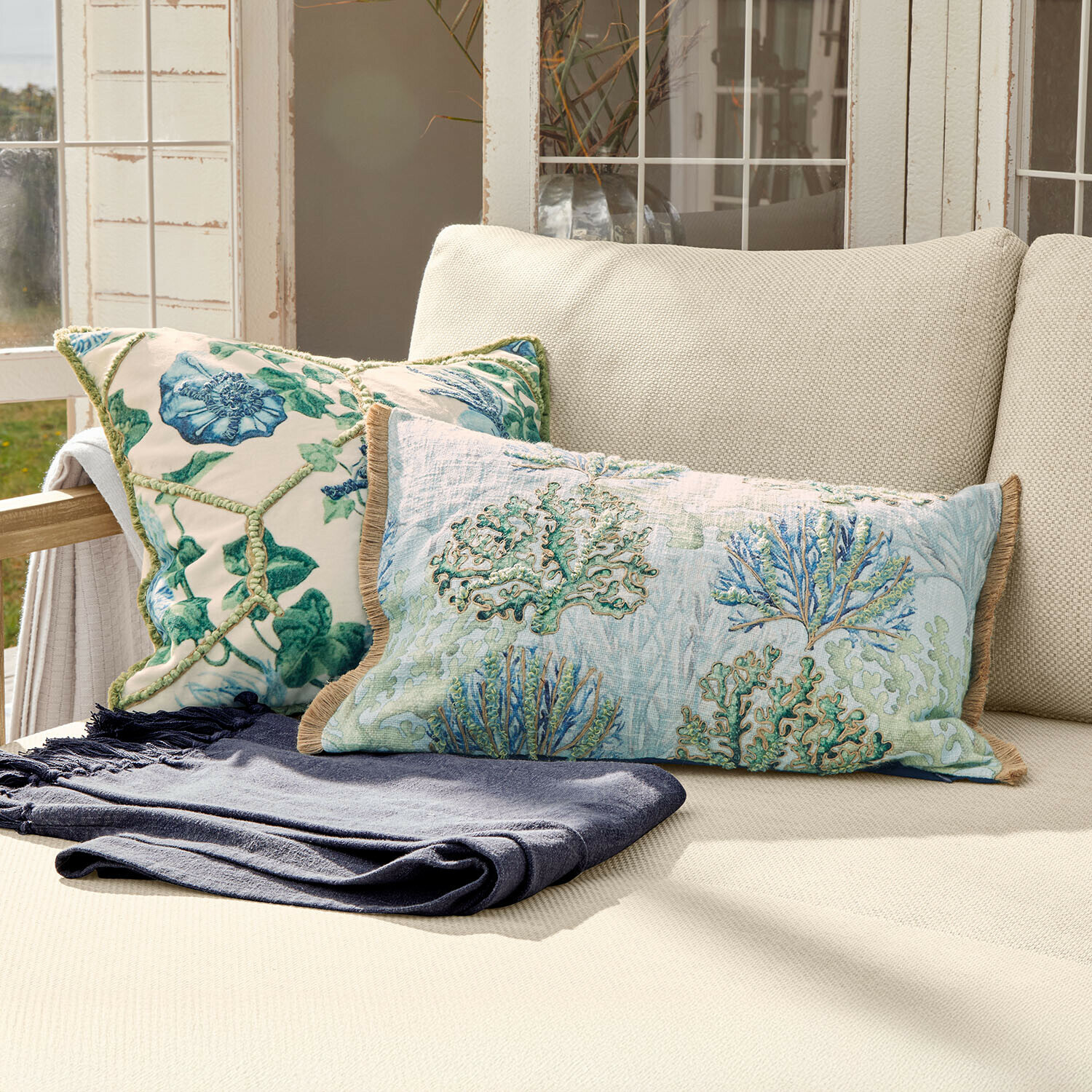 Lot de 2 housses de coussins Ambrisse Coussins décoratifs bicolores à motif végétal sur canapé crème avec plaid bleu marine