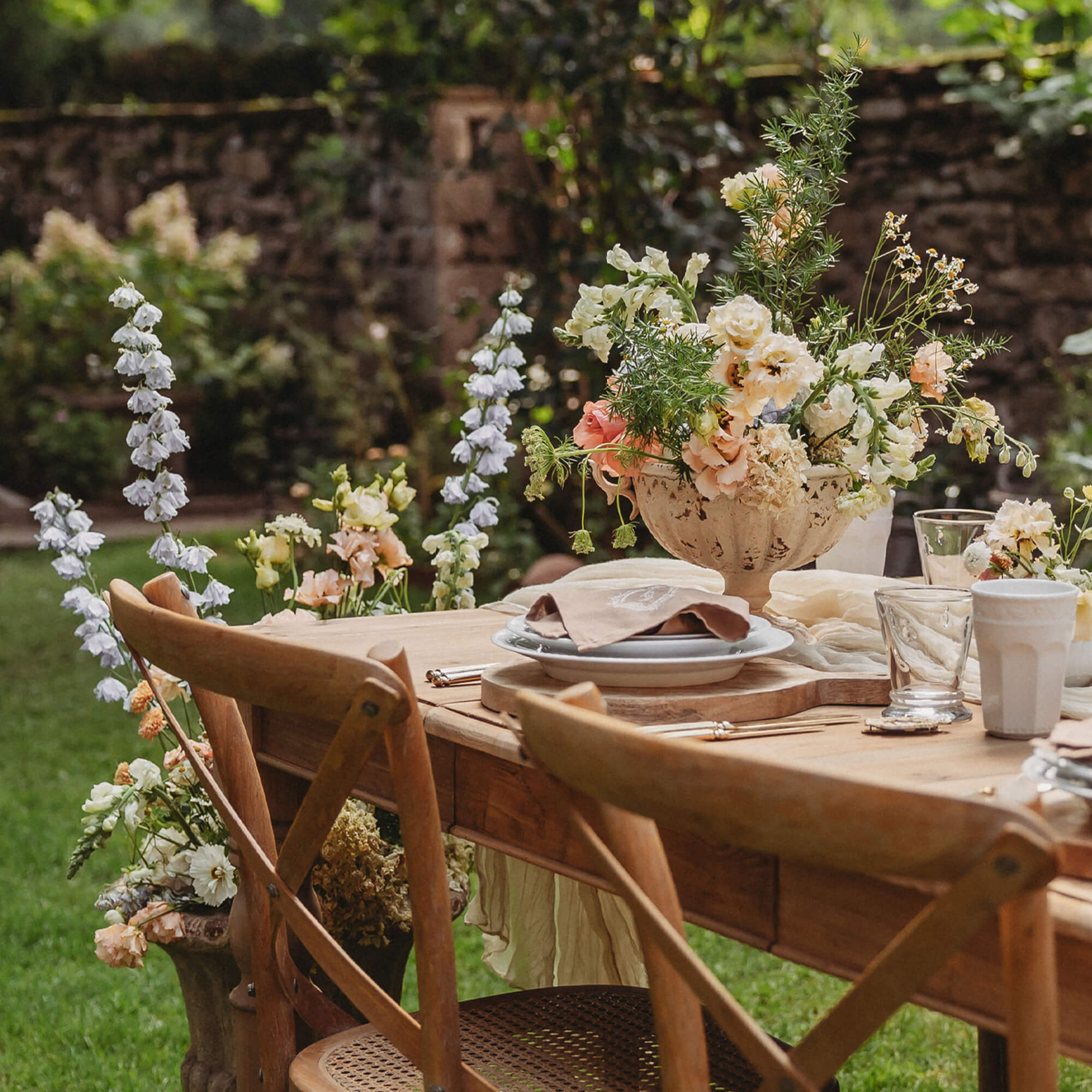 Table de jardin en bois avec décoration florale et chaises naturelles sur pelouse verte