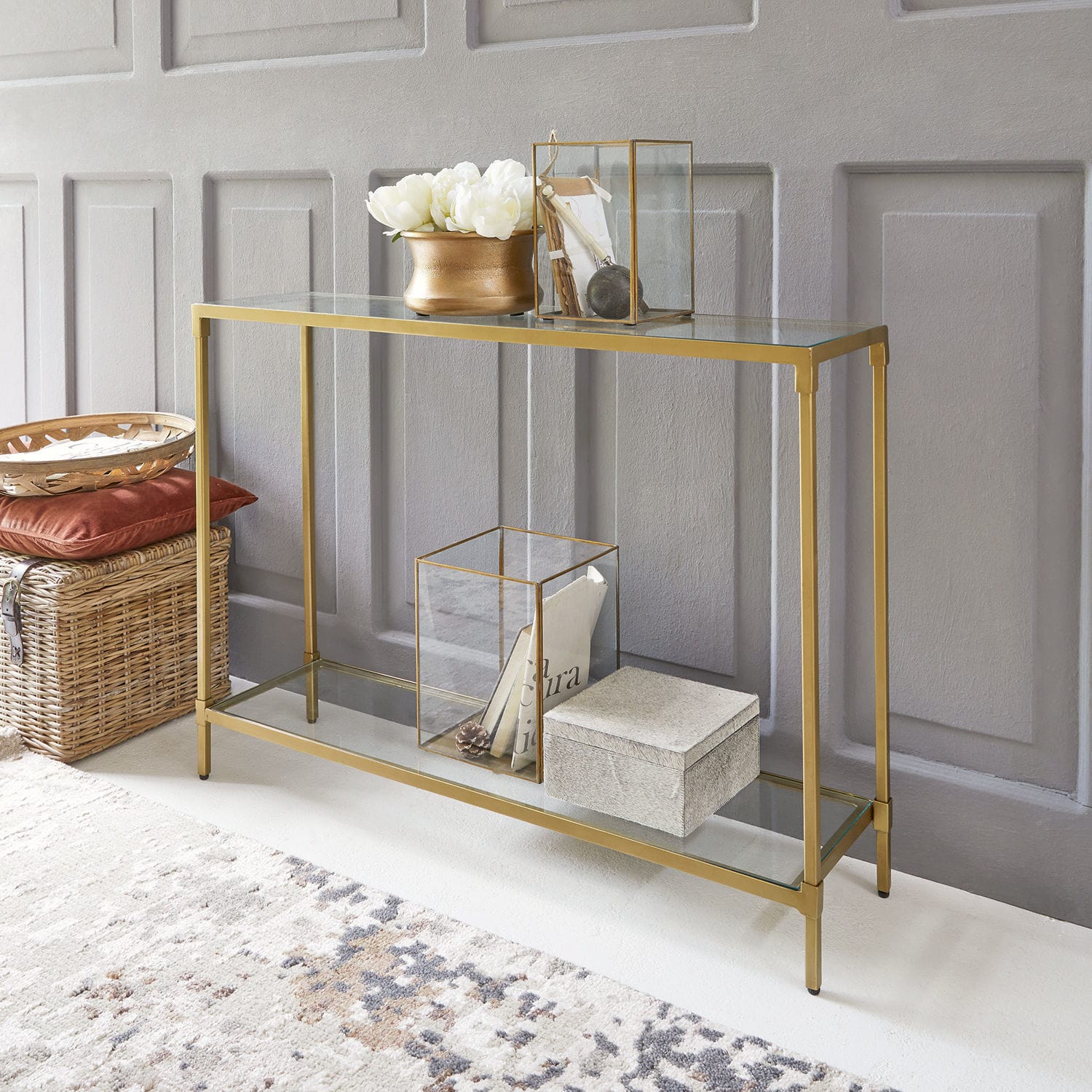 Console Ninove Console en verre avec cadre métallique doré, décorations et panier en osier au sol