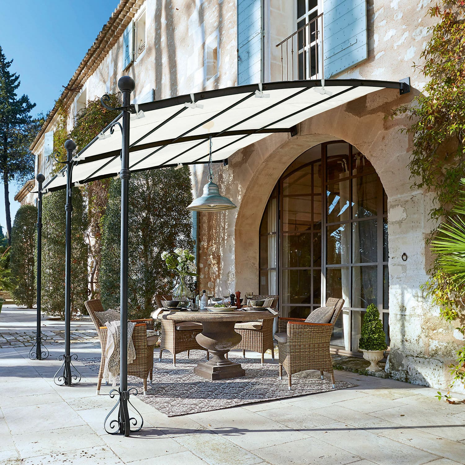 Pergola Kattles Ensemble de meubles de jardin en osier sous un auvent blanc sur une terrasse en pierre devant une maison en pierre