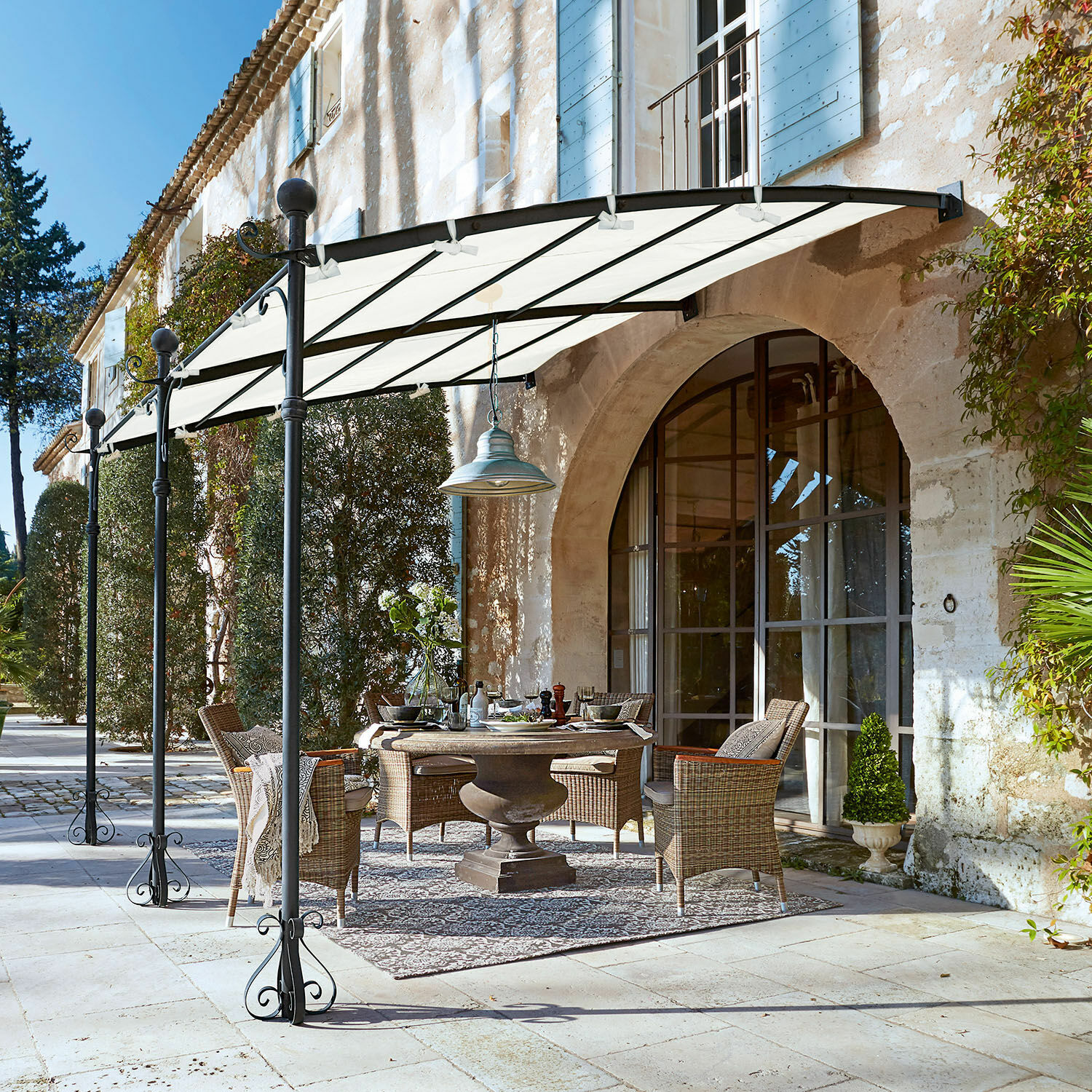 Pergola Kattles Ensemble de meubles de jardin en osier sous un auvent blanc sur une terrasse en pierre devant une maison en pierre