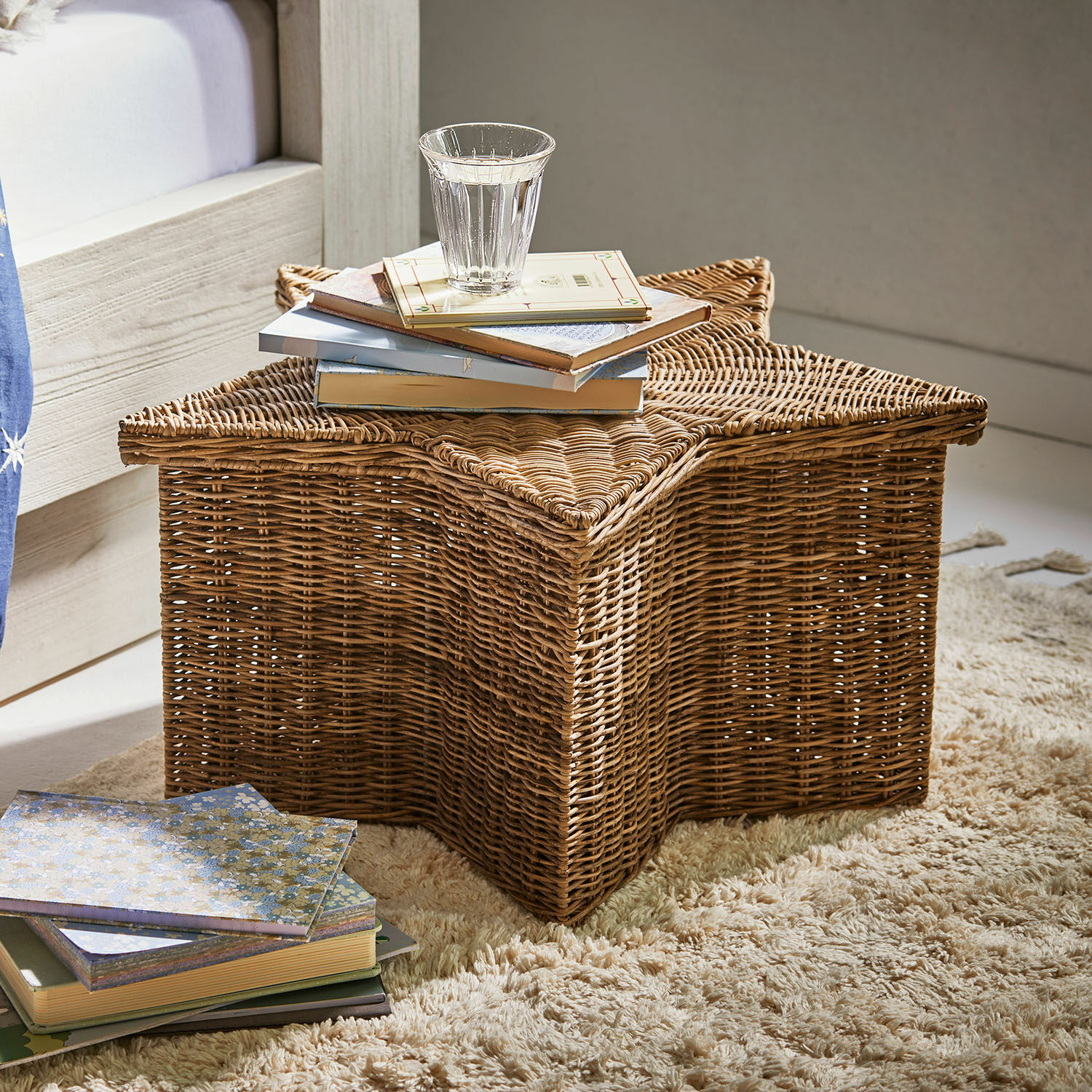 Panier Rivolina Panier en rotin en forme d'étoile sur tapis avec livres et verre d'eau, couleur naturelle