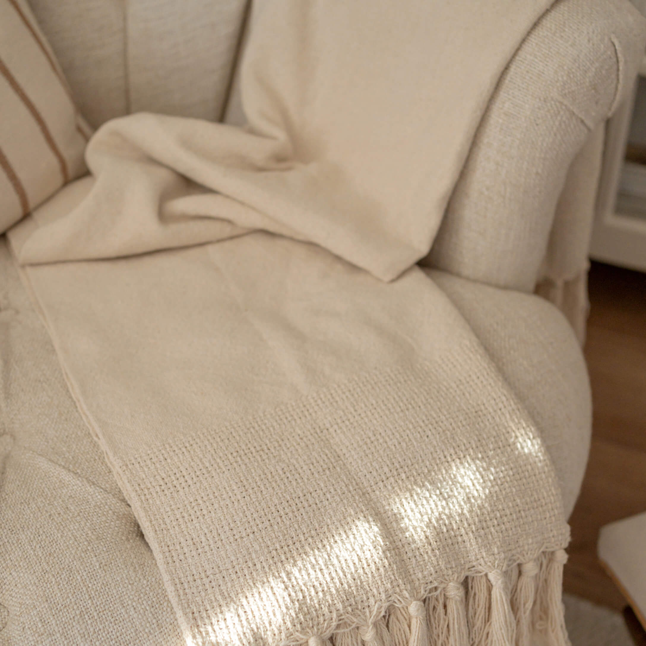 Plaid beige avec franges sur un fauteuil clair, tissu doux pour décoration et confort