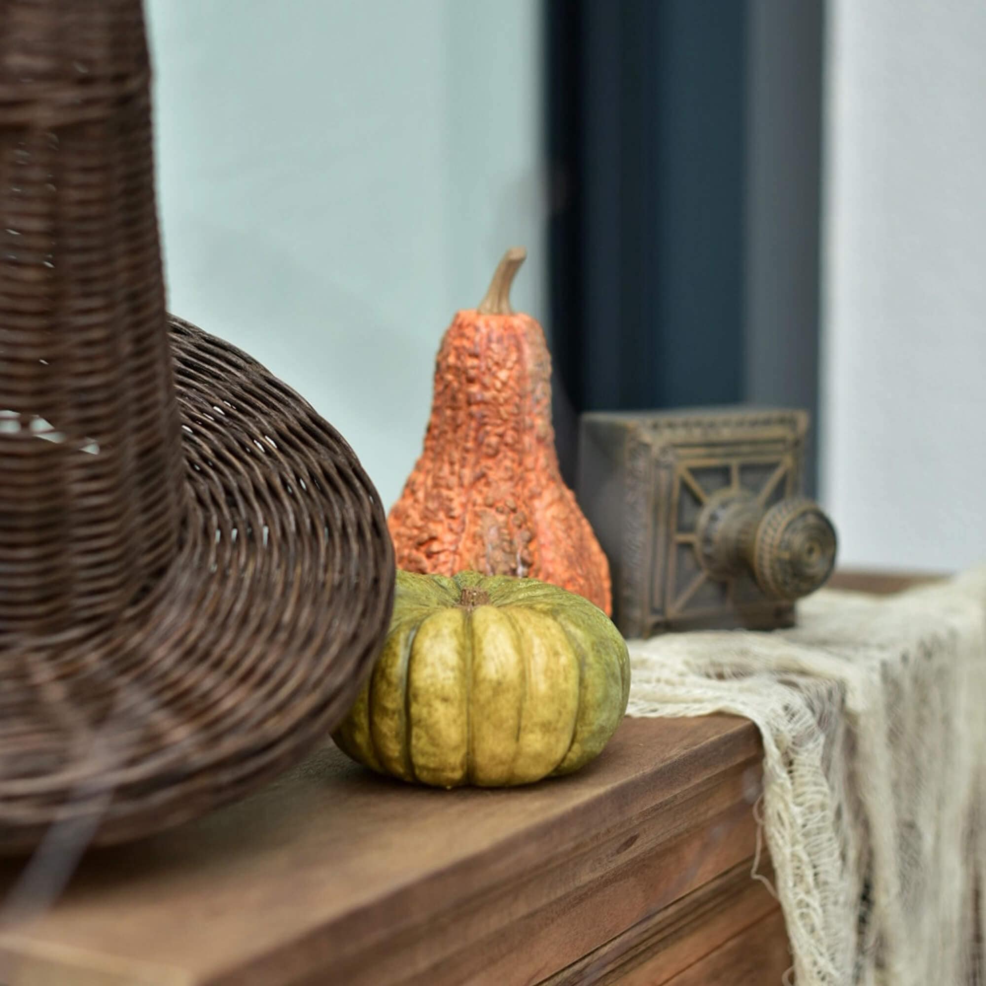 Courges décoratives vertes et orange sur un plateau en bois avec un panier en osier à côté