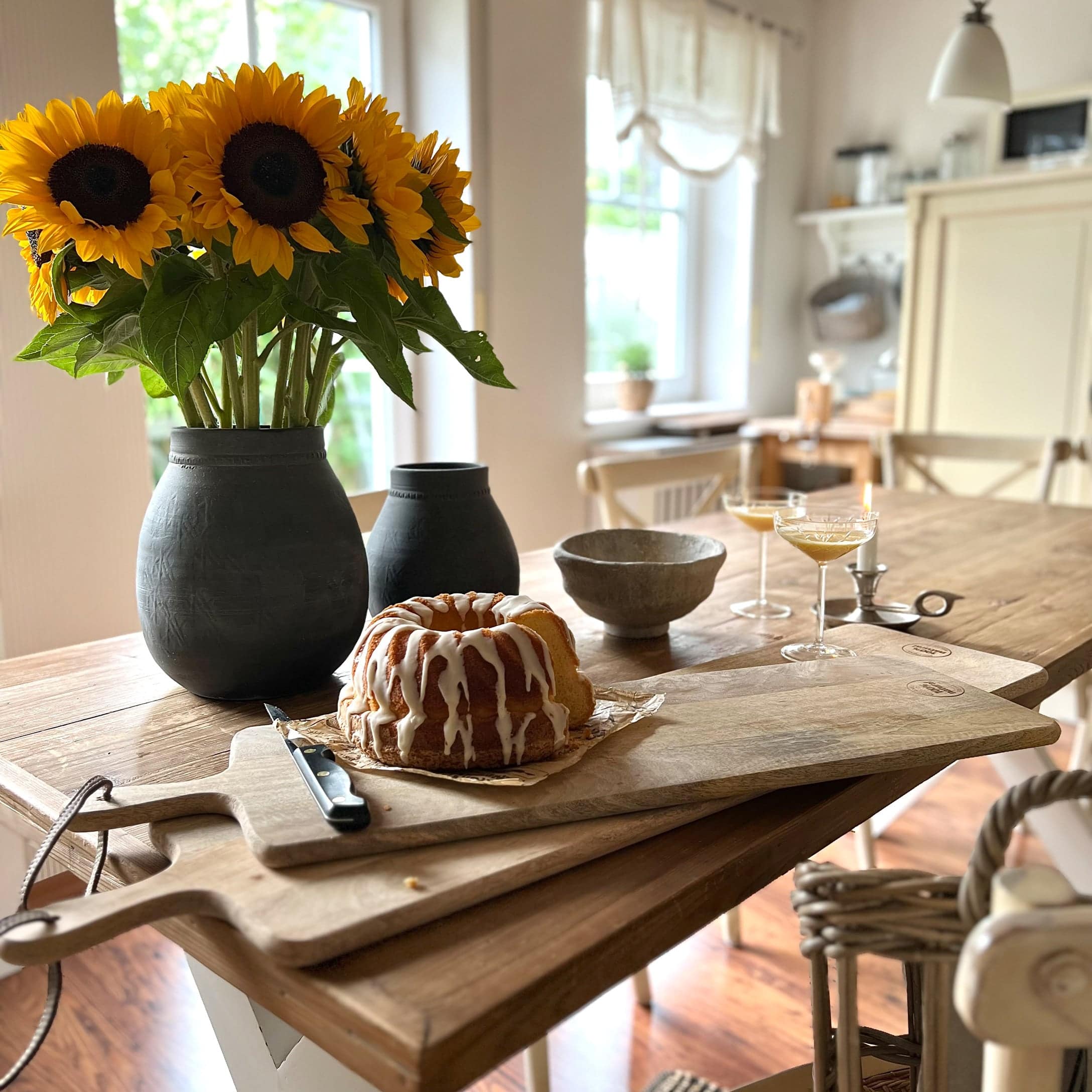 Planche à découper en bois avec gâteau et vase noir contenant des tournesols jaunes sur une table en bois