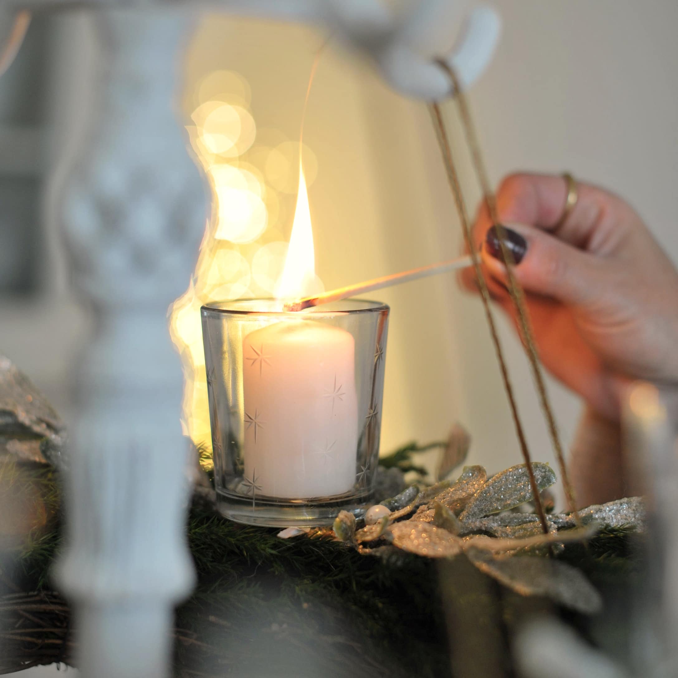 Bougeoir en verre blanc avec motif étoilé et bougie allumée sur couronne de Noël verte