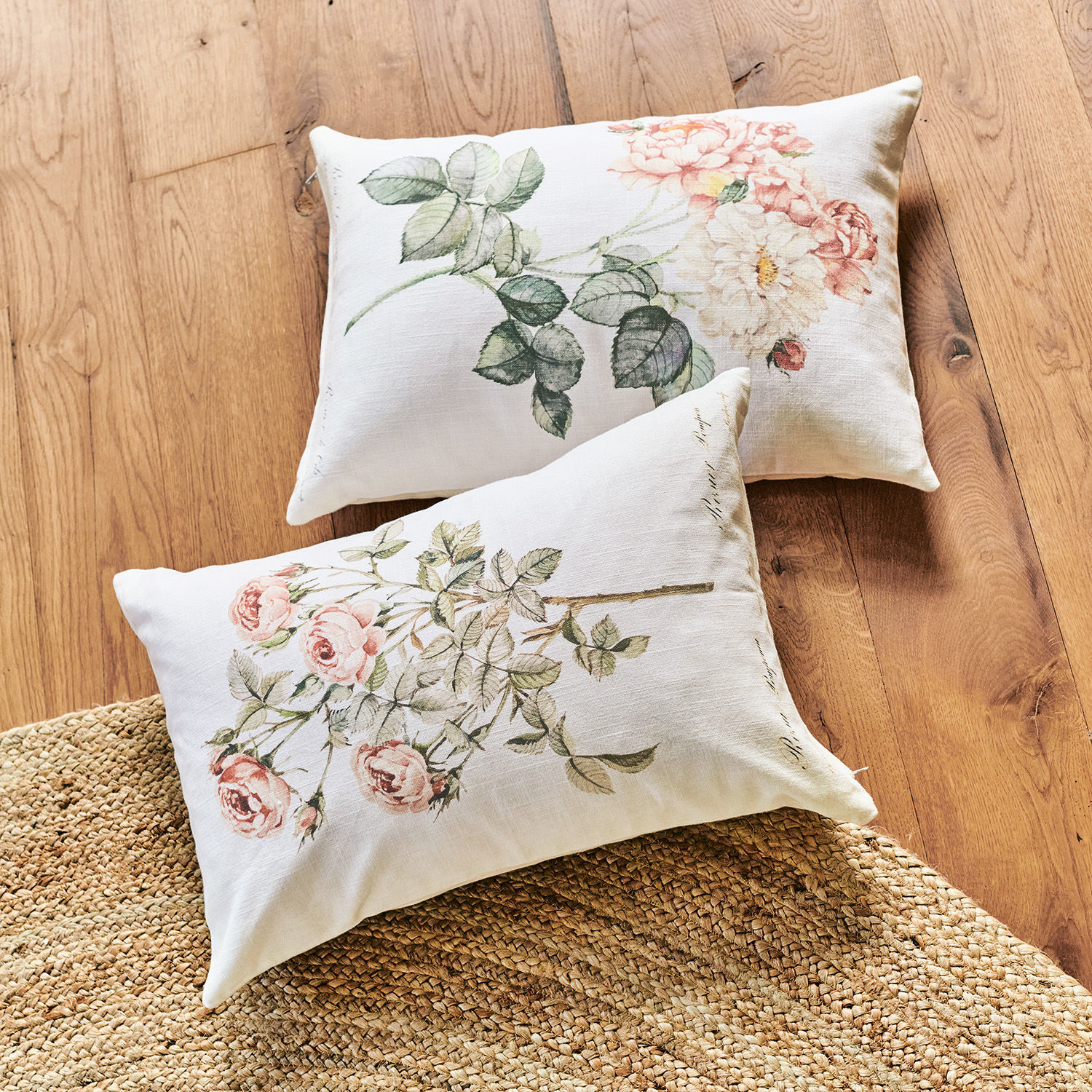 Lot de 2 housses de coussins Girona Deux coussins en lin avec imprimé floral pastel posés sur un sol en bois clair