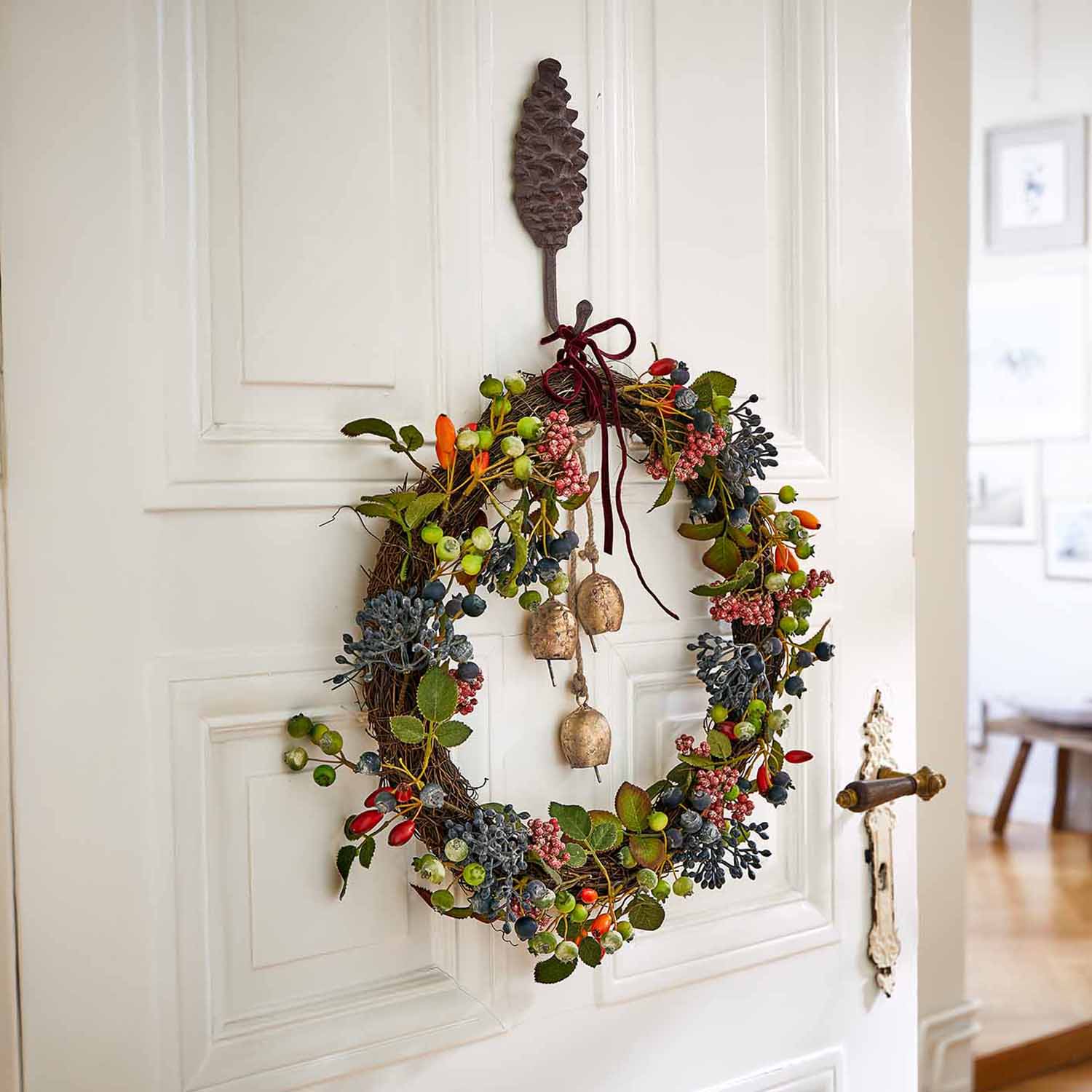 Couronne décorative avec baies colorées et clochettes suspendue à une porte blanche