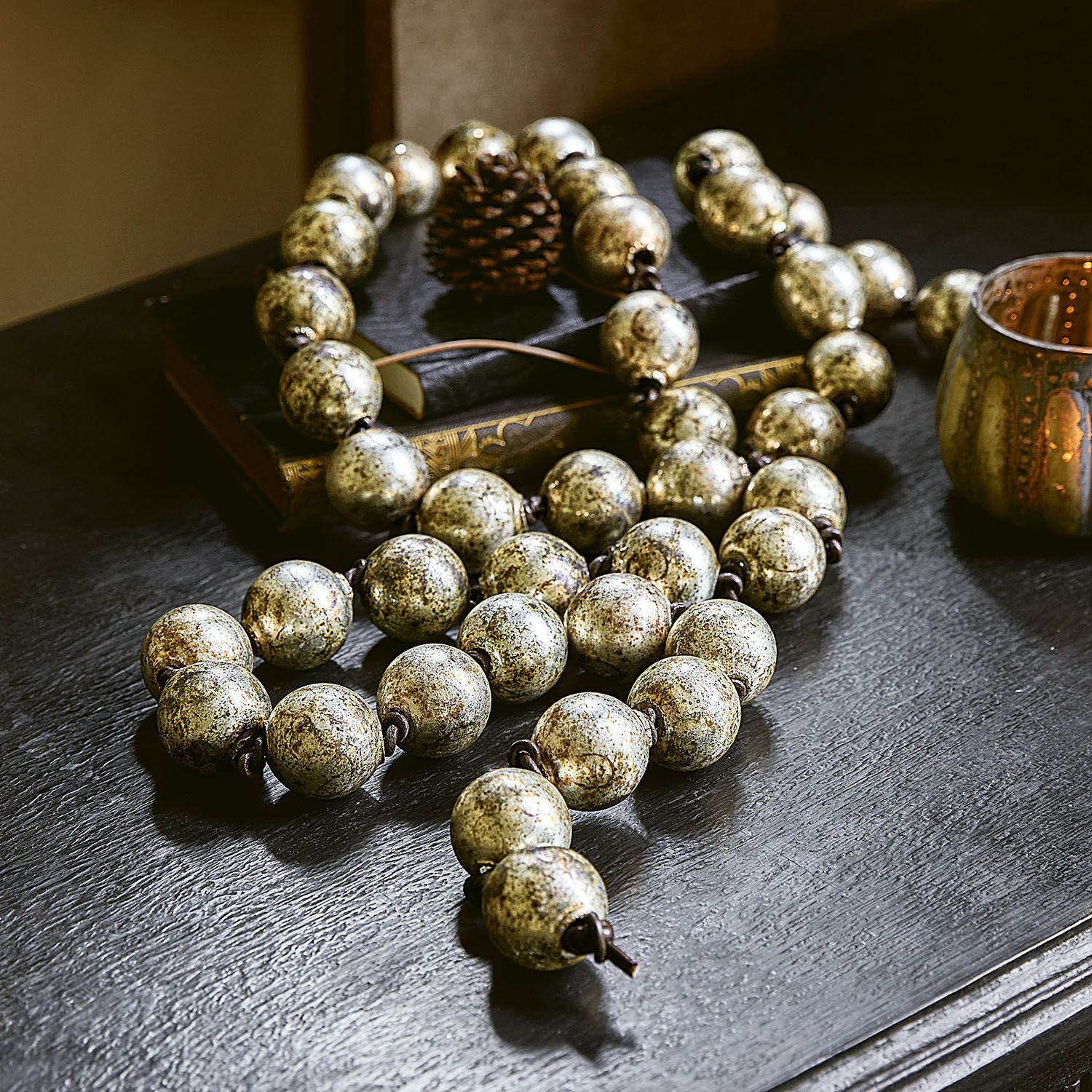 Guirlande Malou Chaîne décorative avec grosses perles dorées vieillies posée sur une table noire avec des livres