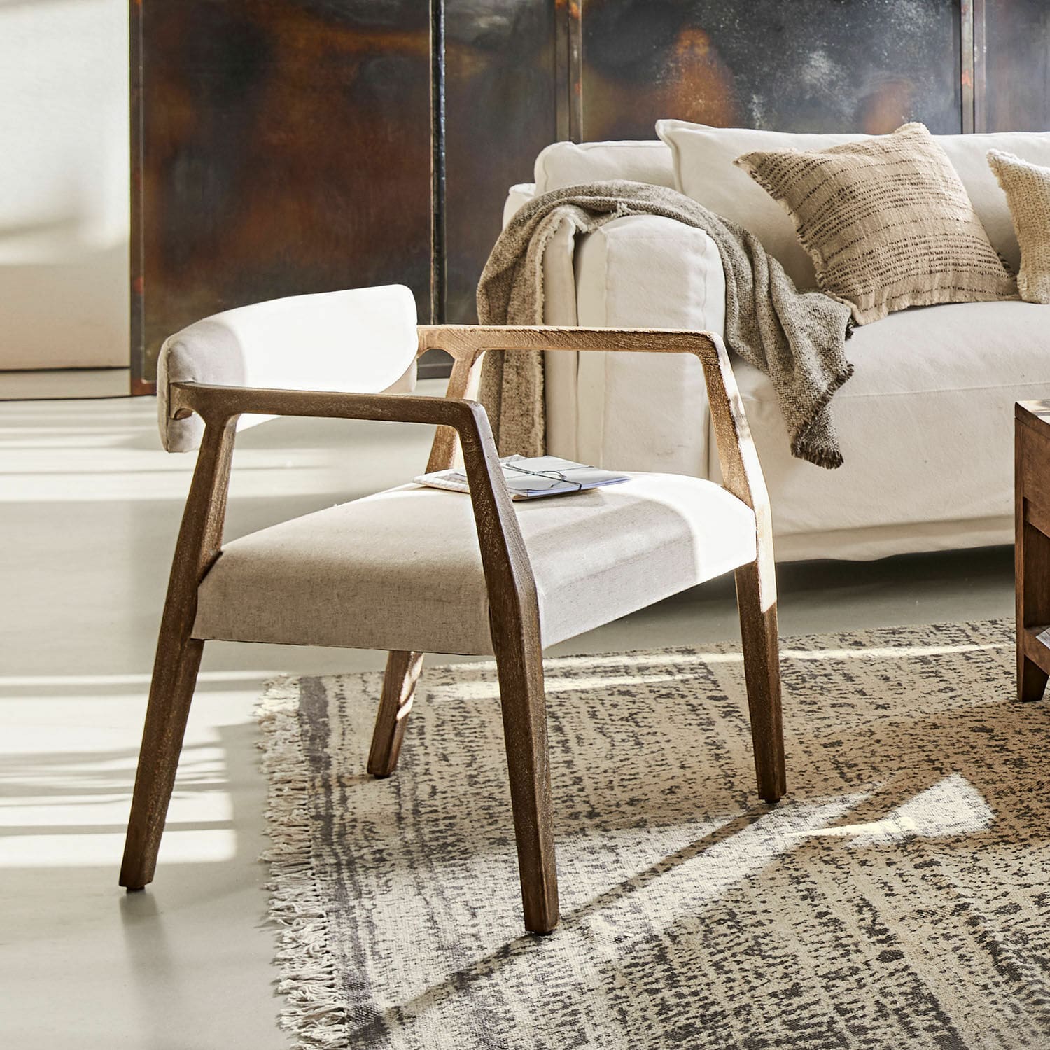 Fauteuil Bronwyn Fauteuil moderne en bois avec assise en tissu clair sur tapis dans un salon lumineux