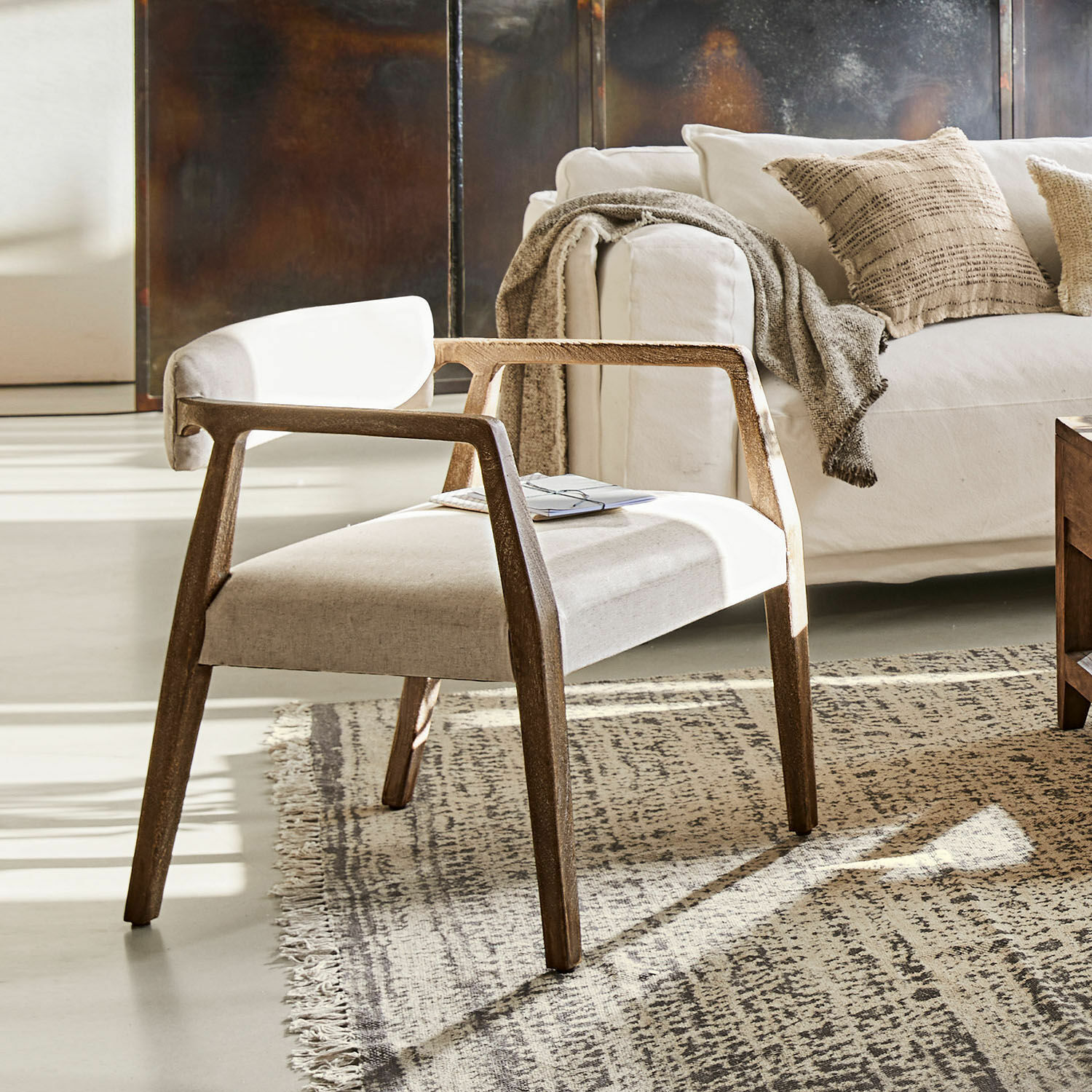 Fauteuil Bronwyn Fauteuil moderne en bois avec assise en tissu clair sur tapis dans un salon lumineux