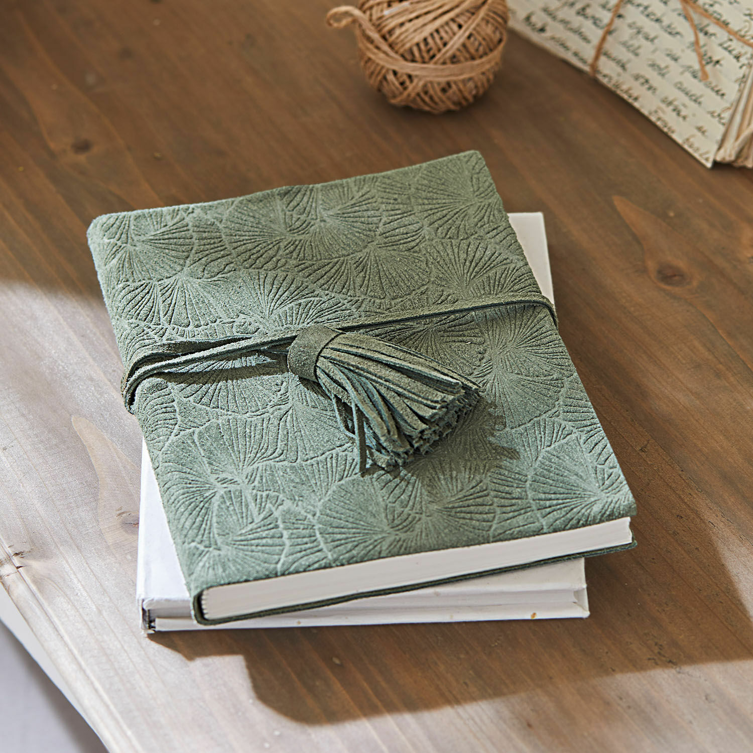 Carnet Brocton Carnet vert en daim avec motif embossé et pompon sur table en bois, accessoires d'écriture