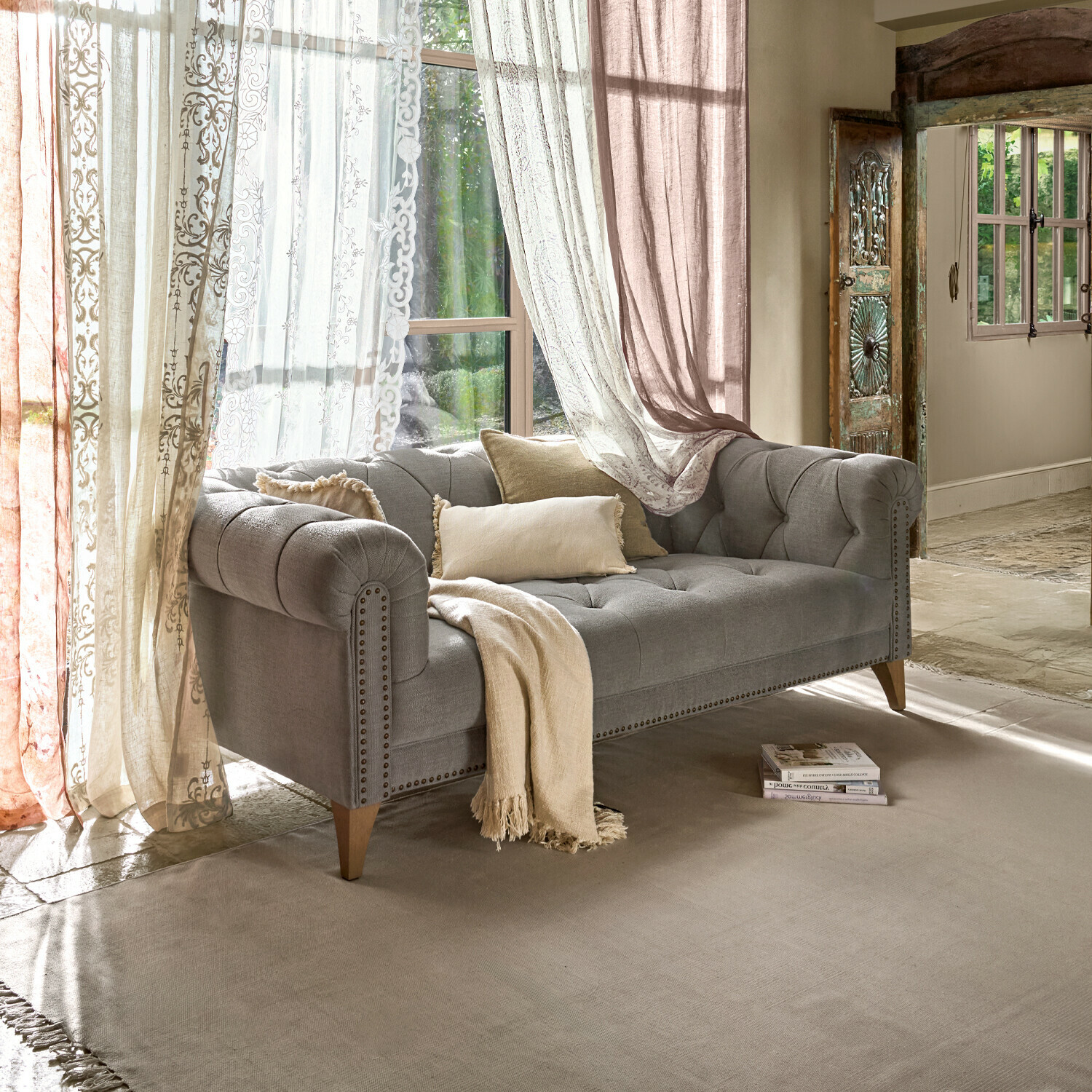 Canapé gris en tissu avec pieds en bois et coussins beiges dans un salon lumineux avec rideaux