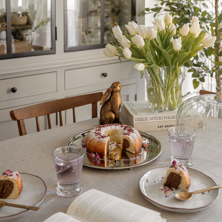 Table avec gâteau marbré sur plateau argenté, tulipes blanches en vase en verre et lapin décoratif