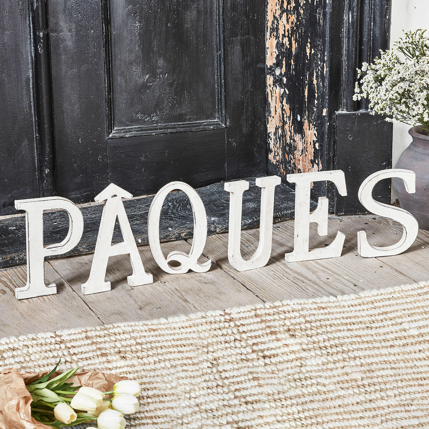 Lettres décoratives PAQUES Lettres décoratives en bois blanc formant le mot Paques sur un sol en bois avec des fleurs
