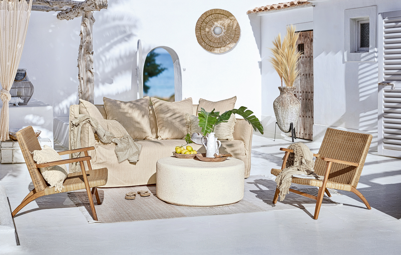 Ensemble de mobilier d'extérieur bohème avec canapé beige et fauteuils en osier sur terrasse lumineuse