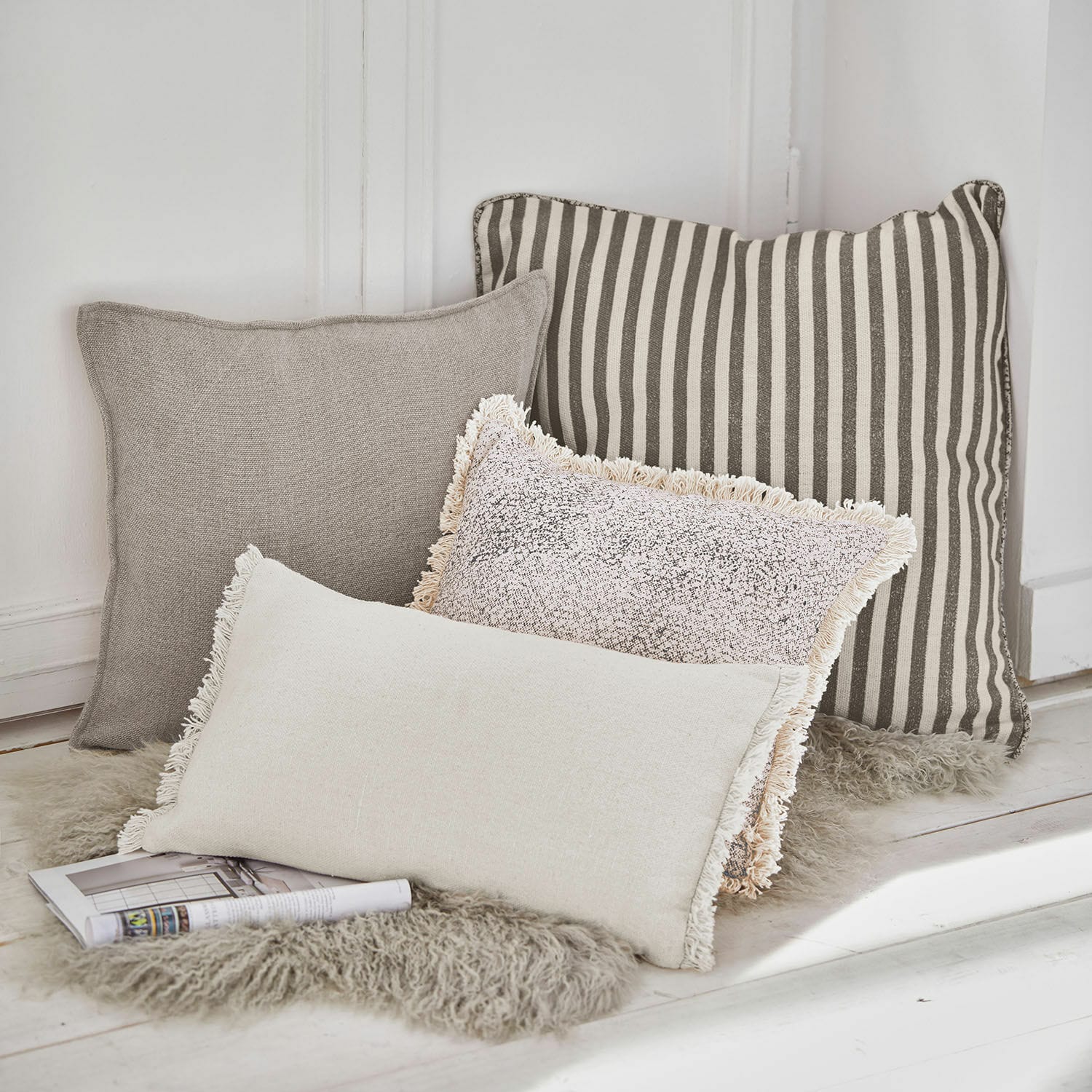 Lot de 4 coussins Valenciennes Ensemble de quatre coussins décoratifs beige et gris posés sur un tapis en fausse fourrure