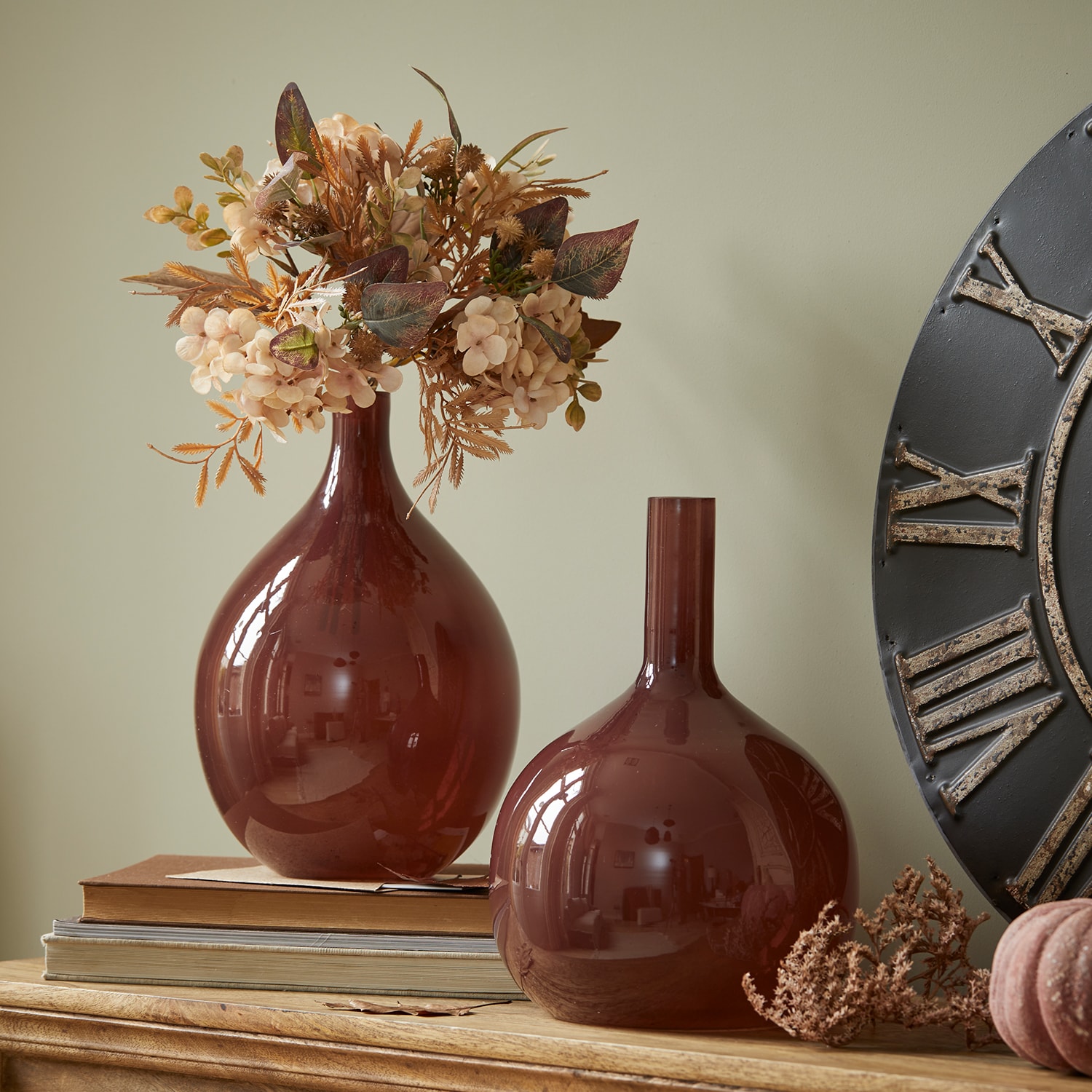 Deux vases décoratifs en verre bordeaux sur une table en bois avec fleurs séchées et livres