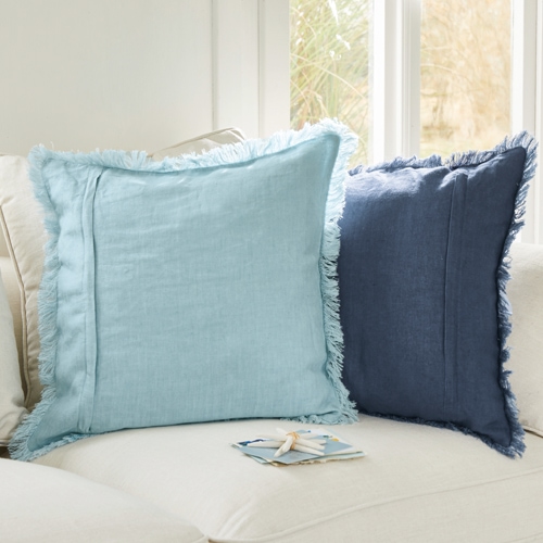 Deux coussins décoratifs en lin avec franges bleu clair et bleu marine sur un canapé clair