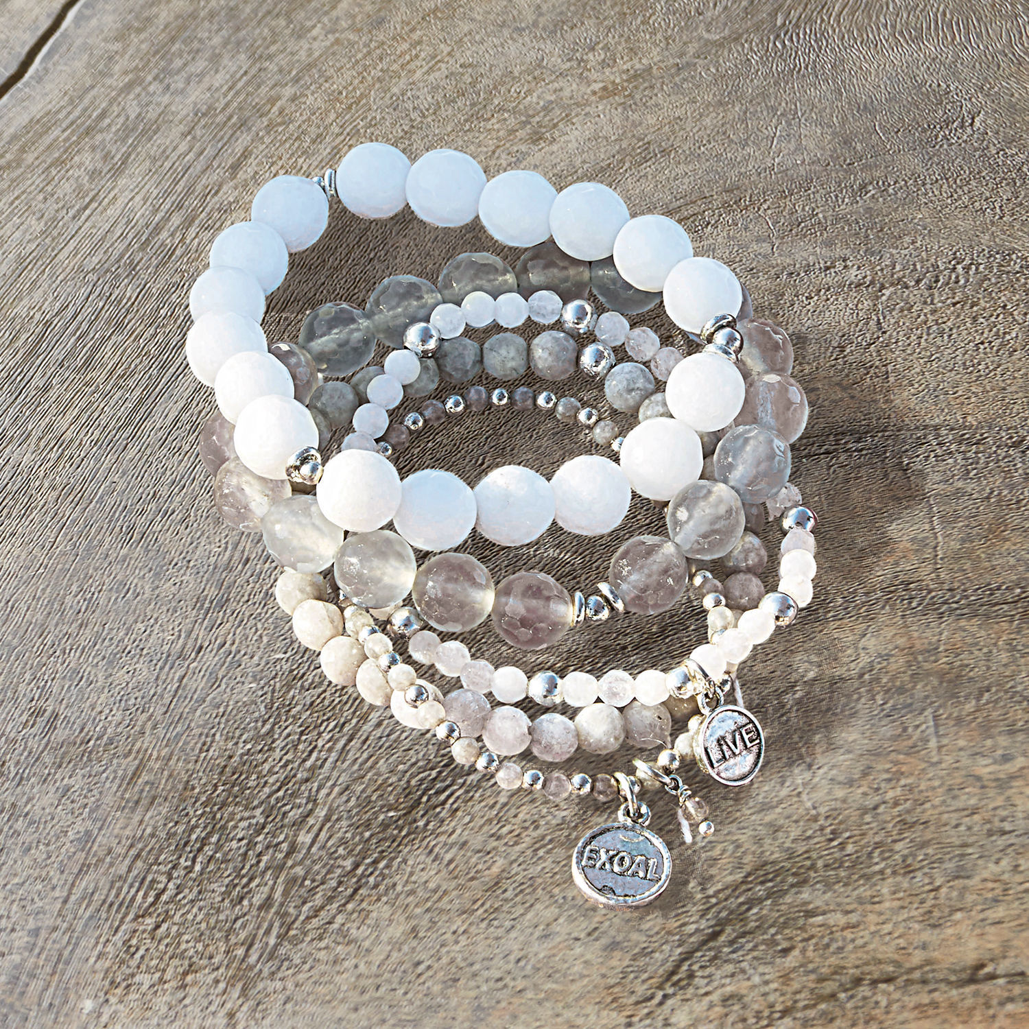 Lot de 5 bracelets Chaim Ensemble de bracelets en pierres blanches et grises avec breloques métalliques sur fond en bois
