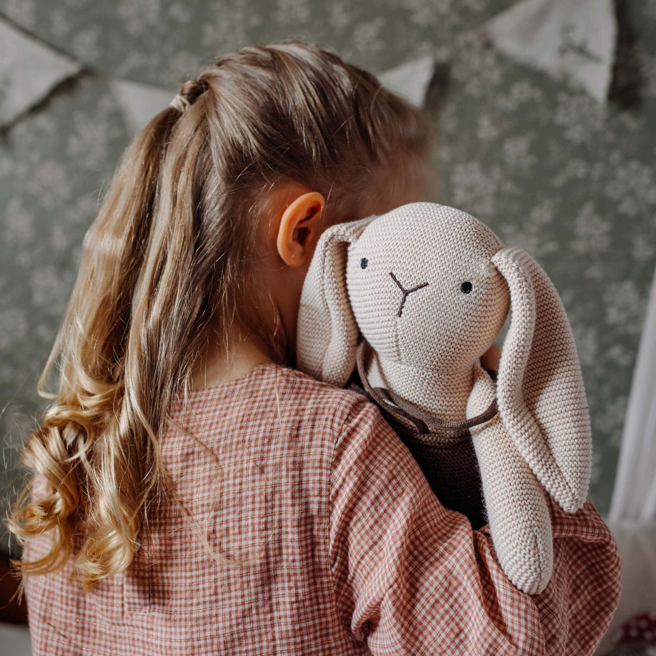 Fille tenant un lapin en peluche tricoté beige dans une chambre d'enfant