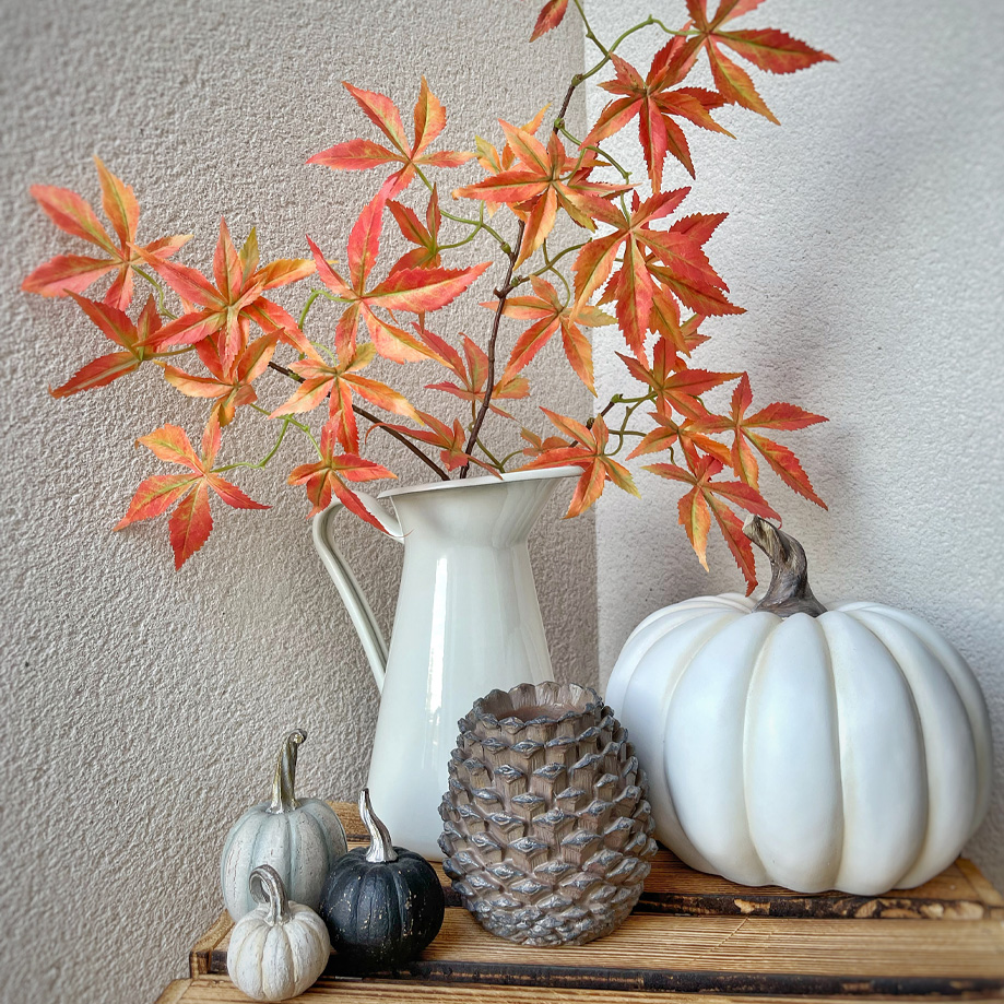Pichet blanc décoratif avec feuilles orange-rouge et citrouilles décoratives sur étagère en bois