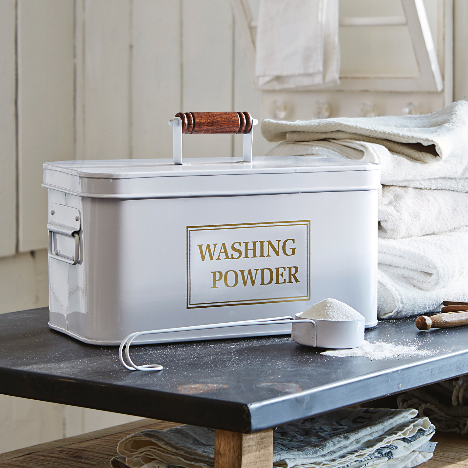 Boîte blanche en métal pour poudre à laver avec poignée en bois et mesurette sur table