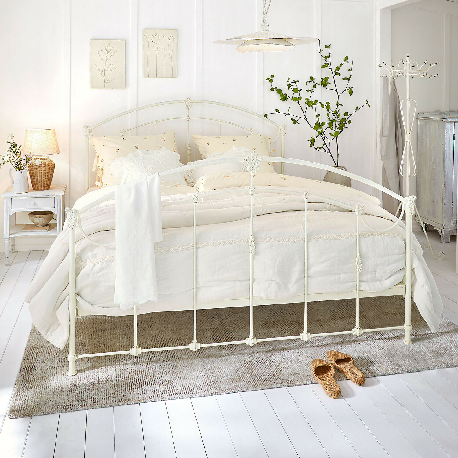 Cadre de lit en métal blanc avec literie crème et tapis naturel dans une chambre lumineuse
