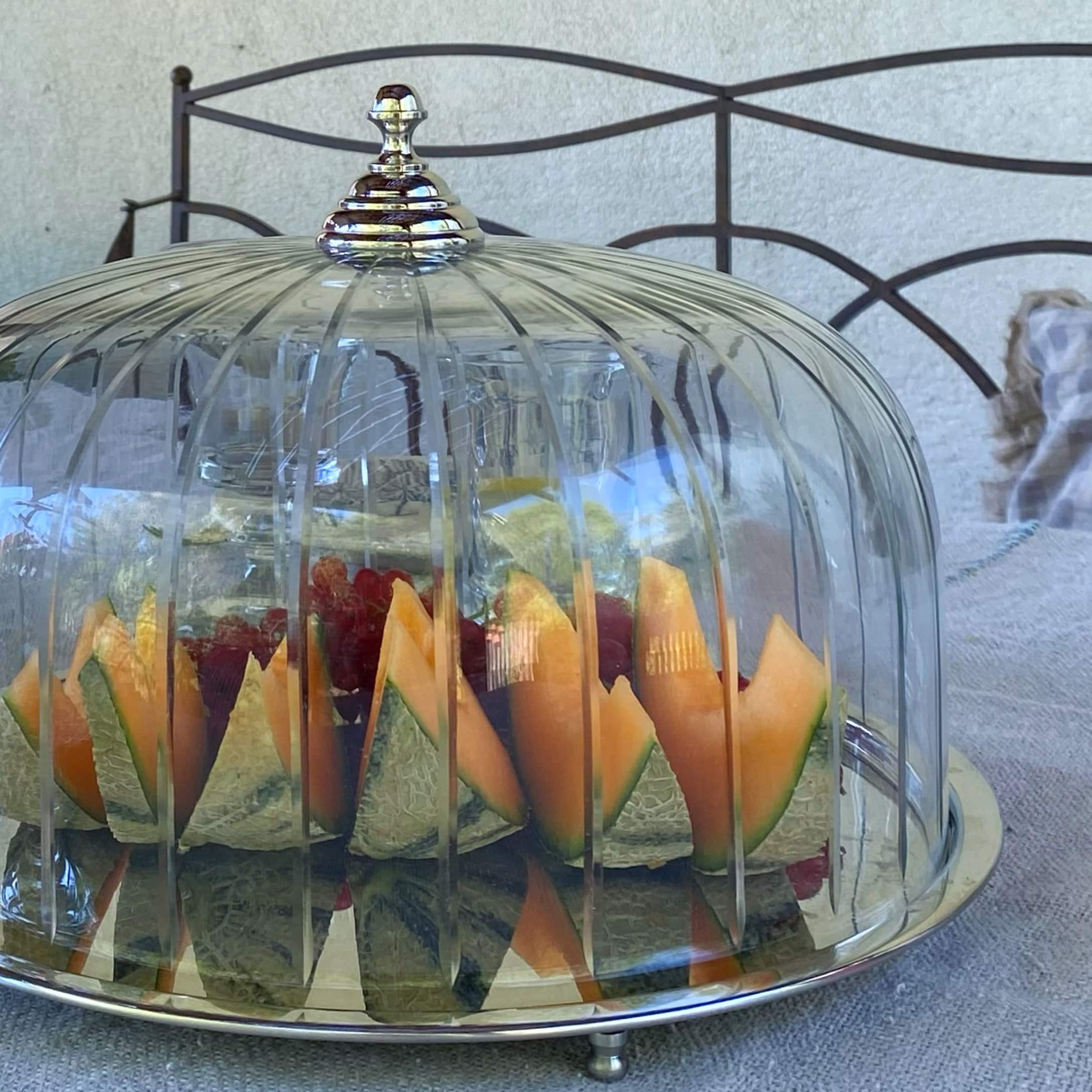Cloche en verre avec plateau métal et fruits frais melon et raisins à l'intérieur sur table
