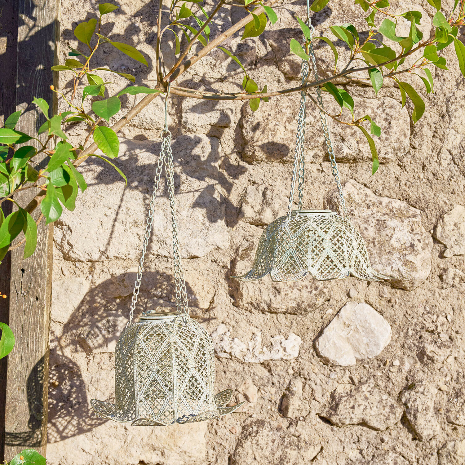 Deux lanternes suspendues en métal gris clair en forme de cloche devant un mur en pierre