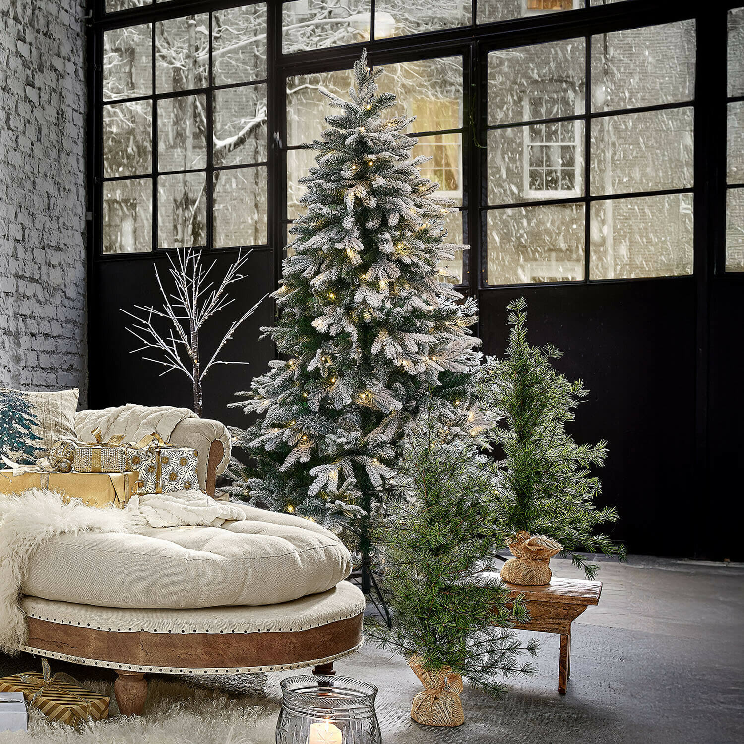 Arbre de Noël Norila Sapin artificiel enneigé avec guirlandes lumineuses dans un salon moderne avec canapé beige et cadeaux